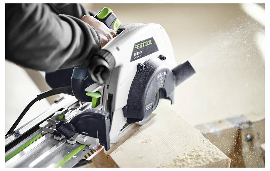 Eine Person arbeitet mit einem Elektrowerkzeug, das mit einem Staubabsaugsystem verbunden ist, auf einer provisorischen Werkbank im Freien in der Nähe eines Gebäudes im Bau.