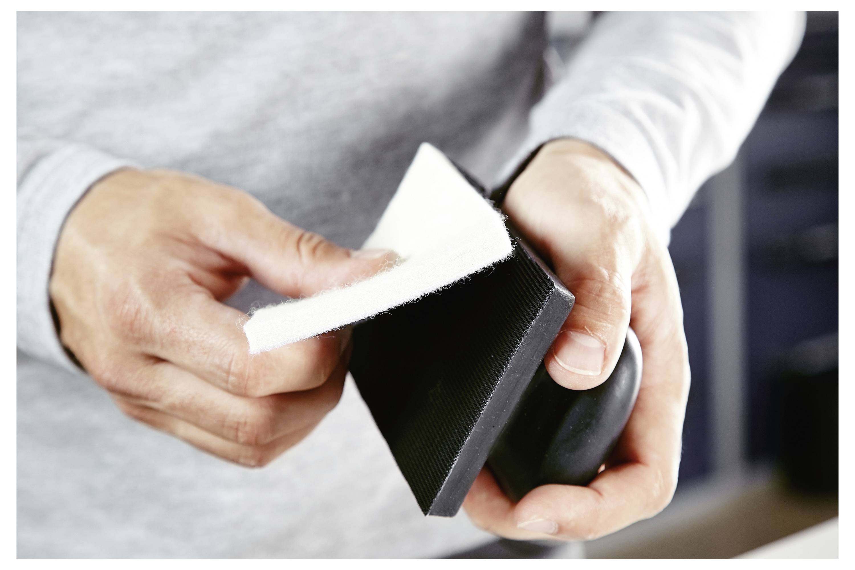 Eine Person hält einen Schleifklotz und Schleifpapier und bereitet sich darauf vor, eine Oberfläche zu glätten.