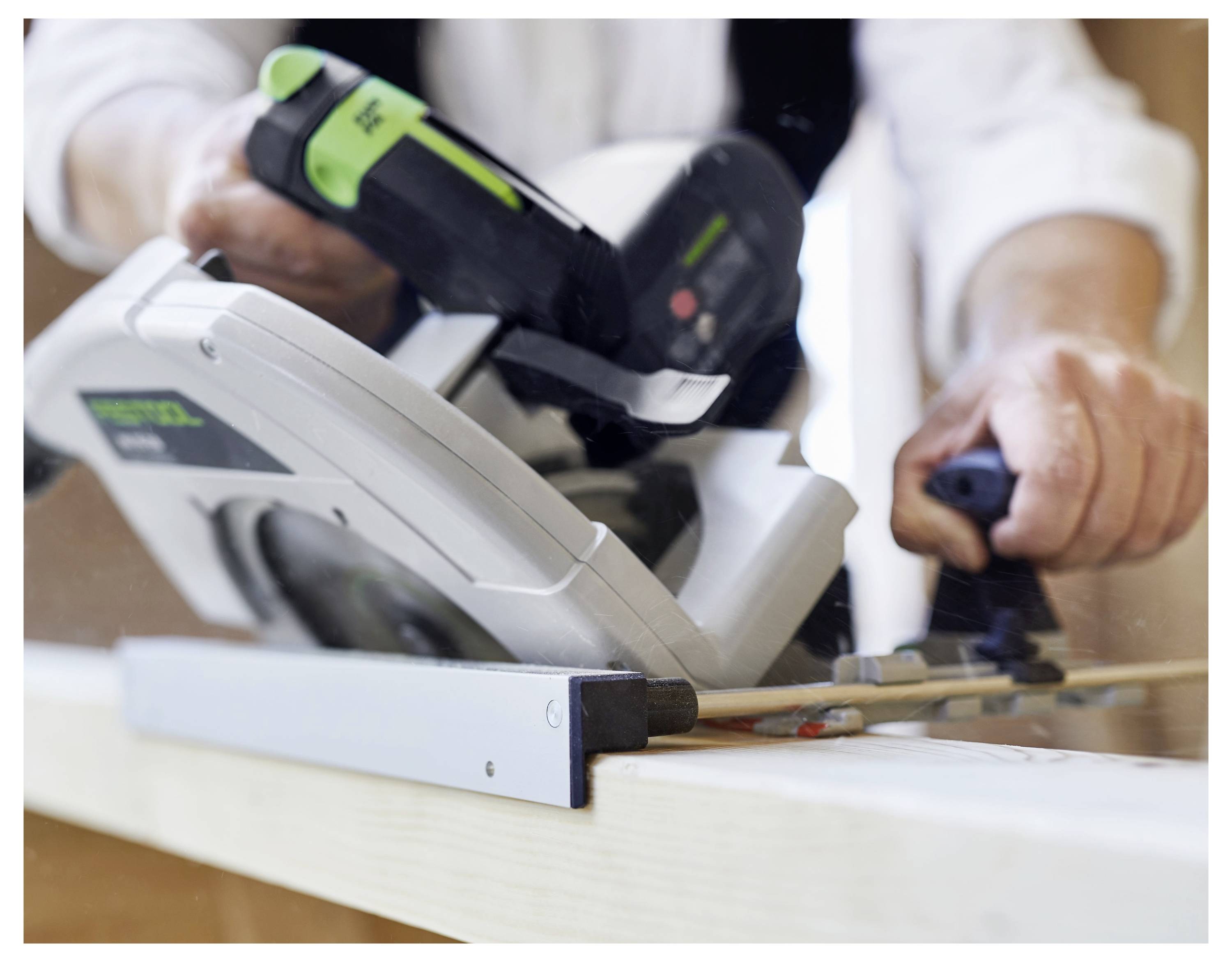 Eine Person, die mit einer Kreissäge Holz schneidet und fest hält. Die Säge wird von einer grün-schwarzen Batterie angetrieben und zeigt Bauarbeit.