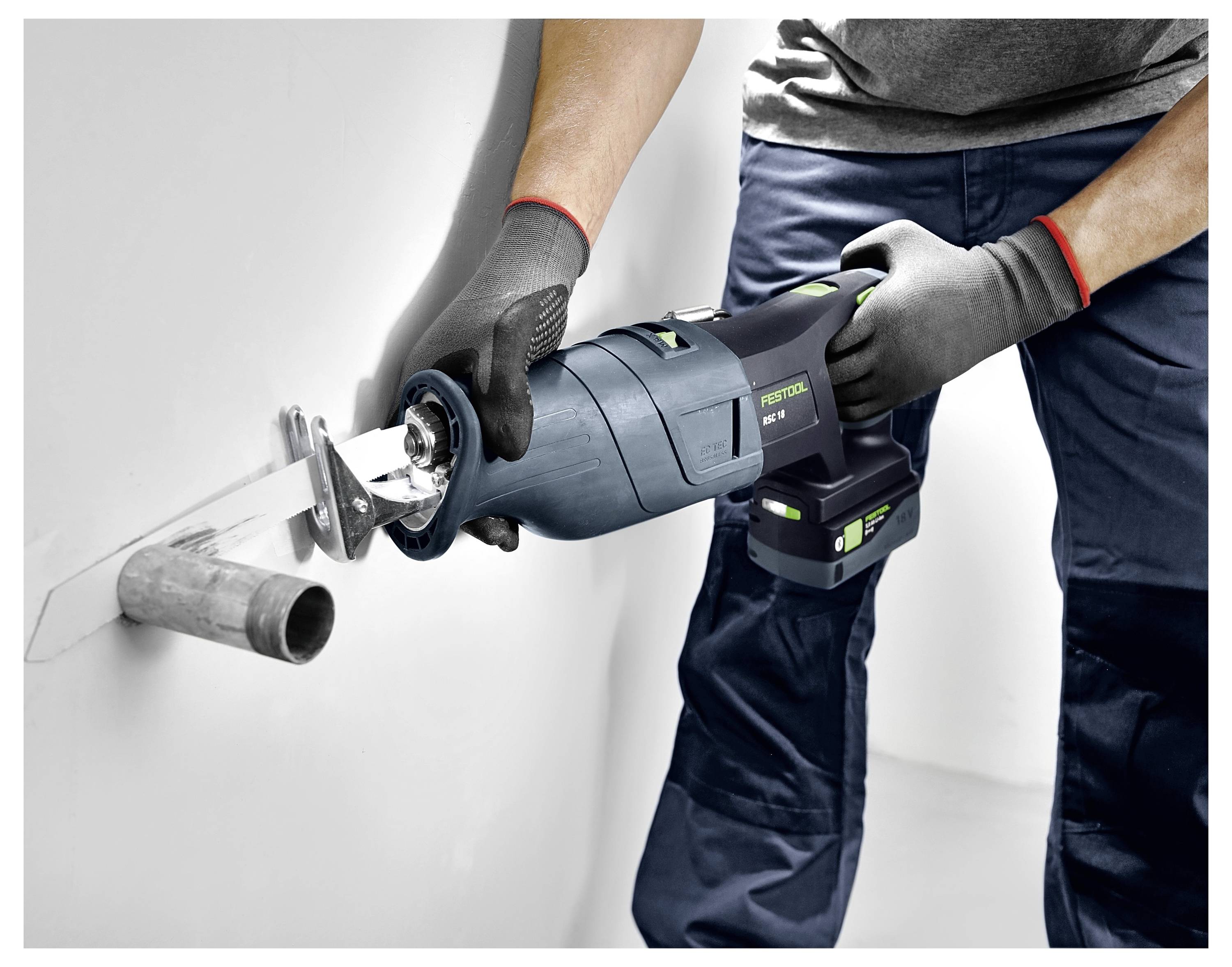 Eine Person in Schutzhandschuhen nutzt ein Elektrowerkzeug, um ein aus der Wand herausragendes Metallrohr zu durchtrennen, was auf eine sanitärtechnische oder Bauaufgabe hindeutet.