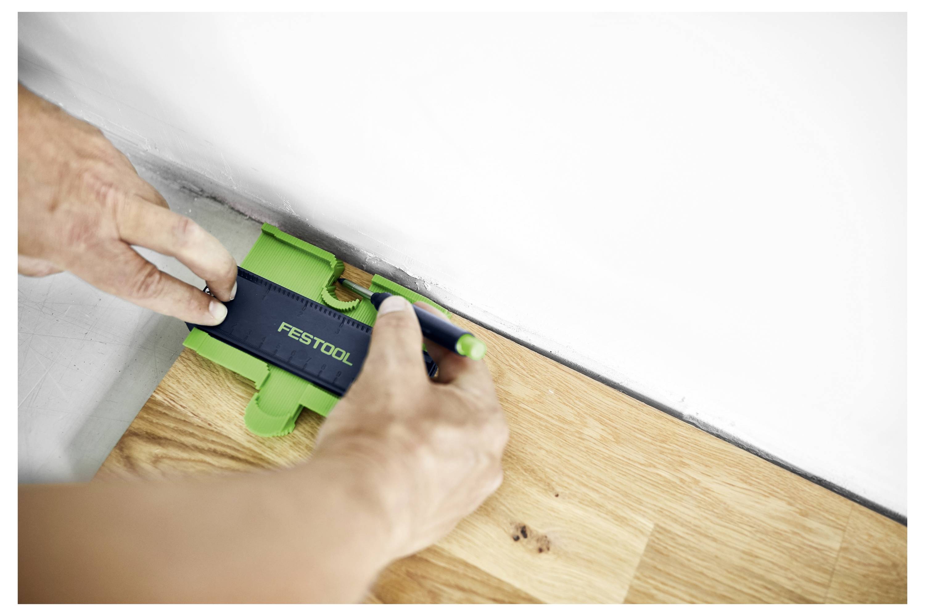Hand benutzt ein Konturlehre zum Messen einer Ecke auf einem Holzboden für präzises Schneiden.