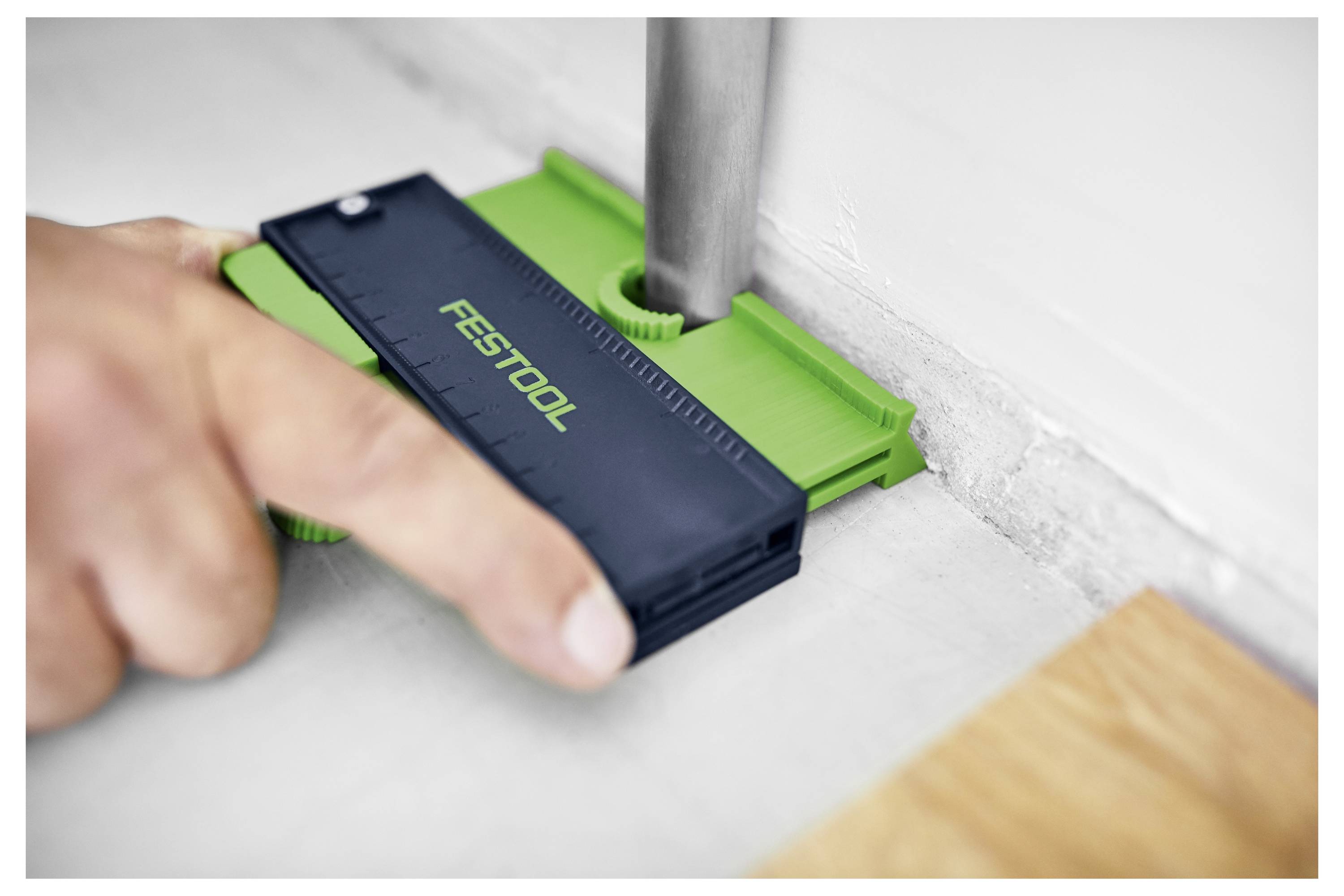 Eine Hand nutzt eine Festool-Konturlehre, um die Form eines Rohrs gegen eine Wand genau zu messen und zu replizieren.