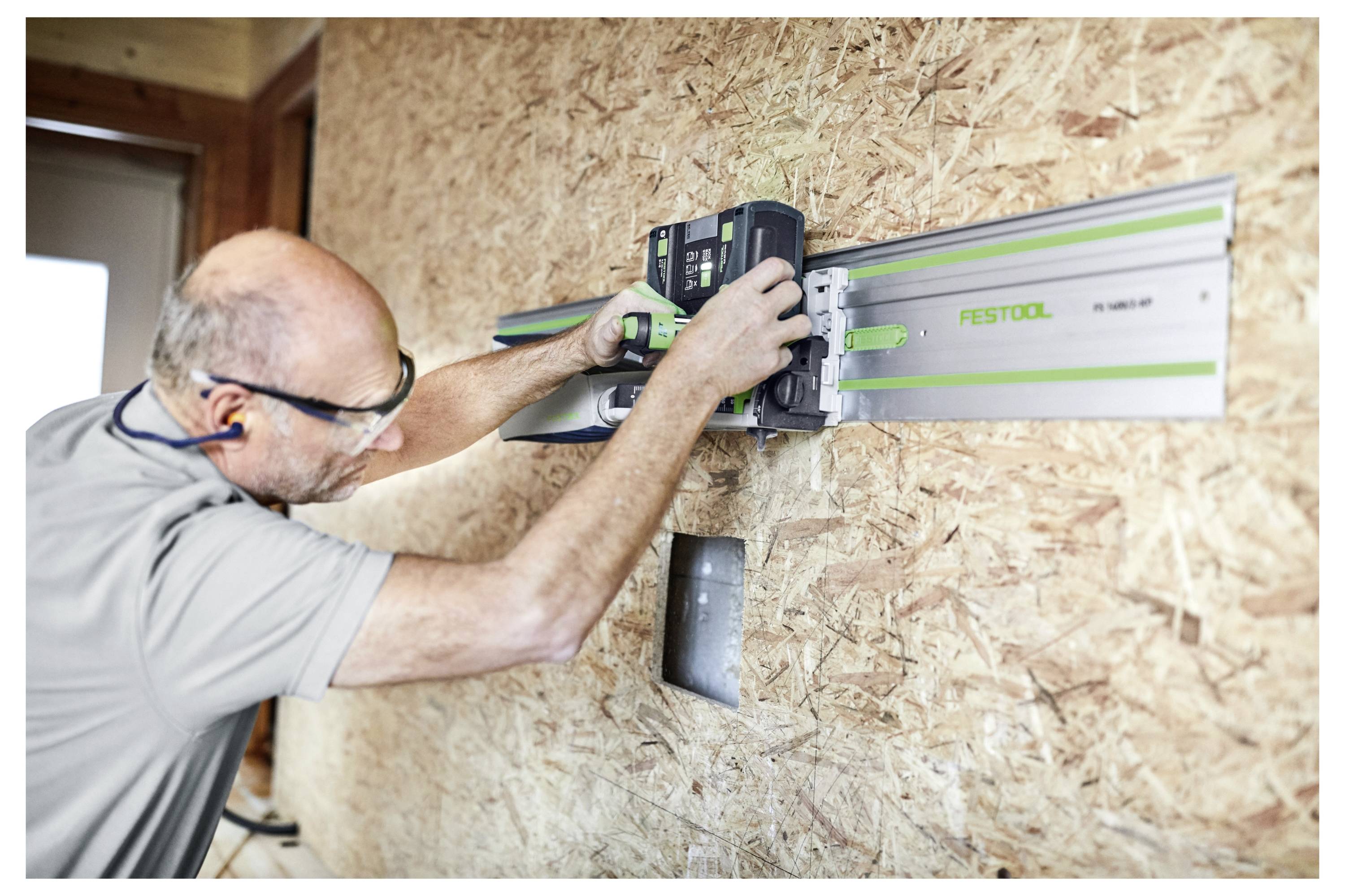 Eine Person, die ein Holzbearbeitungswerkzeug verwendet, um Holz auf einer strukturierten Wand zu ebnen oder zu schneiden, wobei sie zum Schutz eine Schutzbrille trägt.