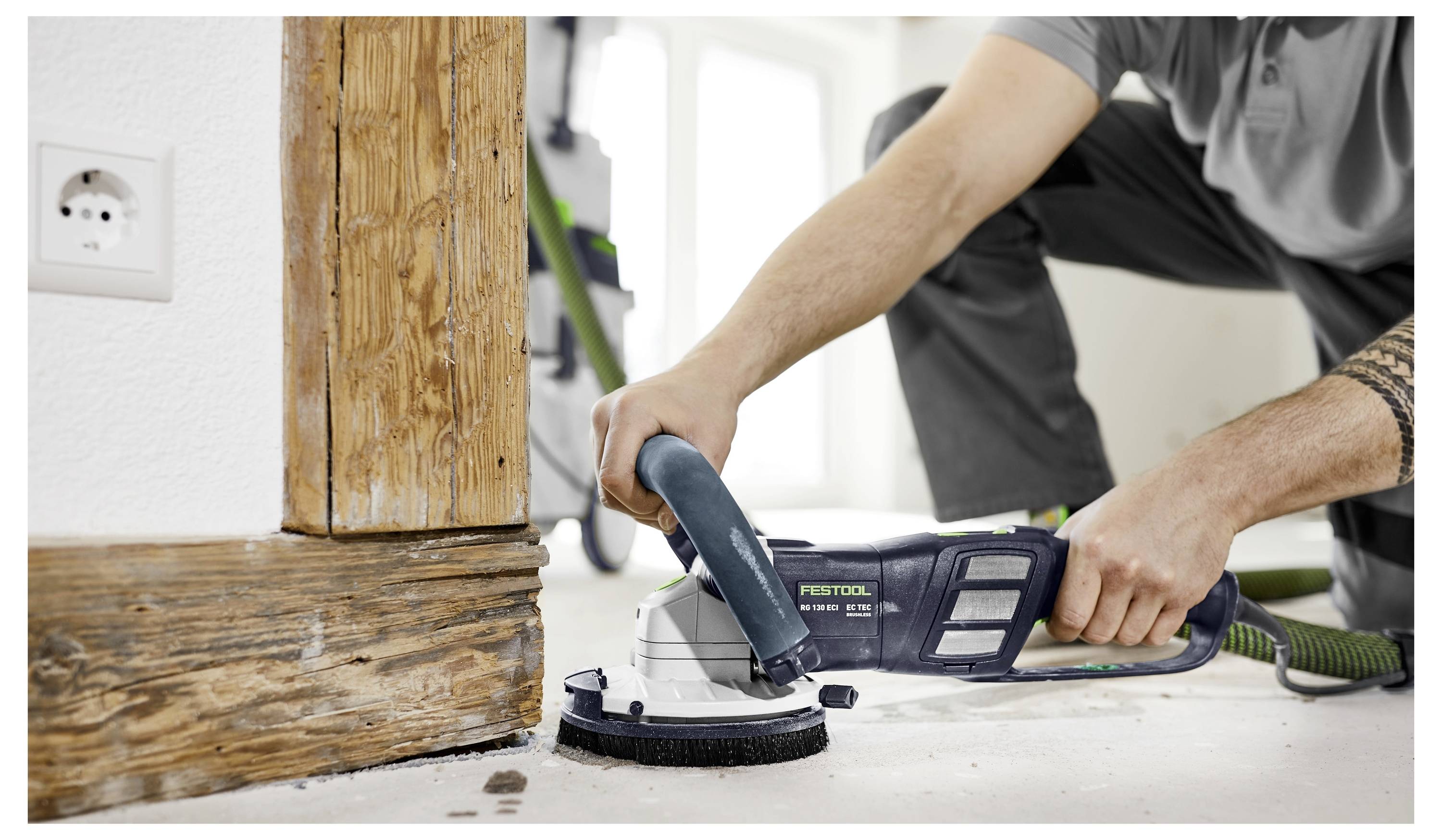 Eine Person nutzt ein Elektrowerkzeug, um die untere Ecke einer Holztürrahmens in einem Zimmer abzuschleifen.