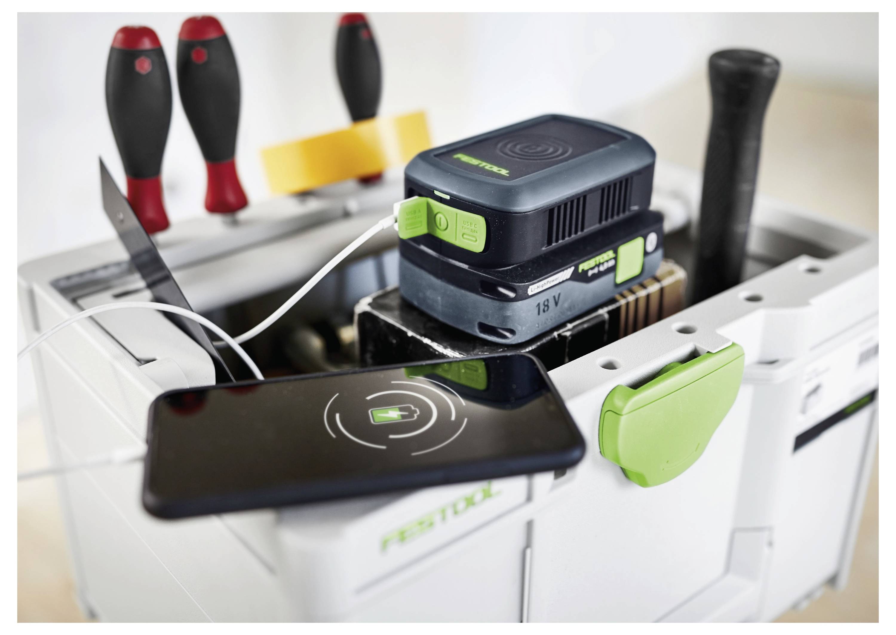 Eine Ladestation enthält verschiedene Werkzeuge. Ein Smartphone, das mit einem Kabel angeschlossen ist, ruht oben auf der Station. Bohrmaschinen und Elektrowerkzeuge sind sichtbar.