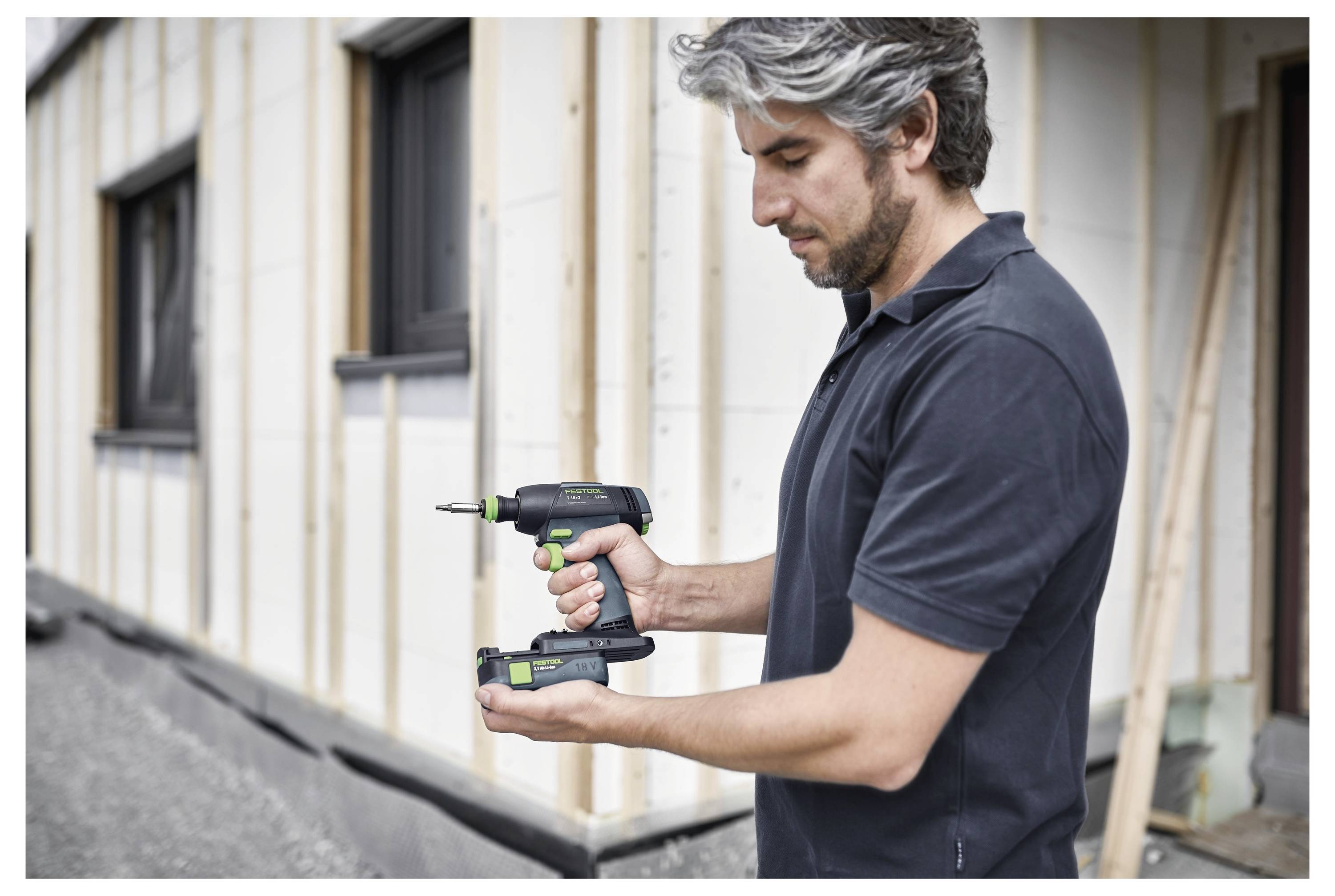 Eine Person, die auf einer Baustelle einen Elektroschrauber benutzt, steht neben einem Gebäude im Bau.