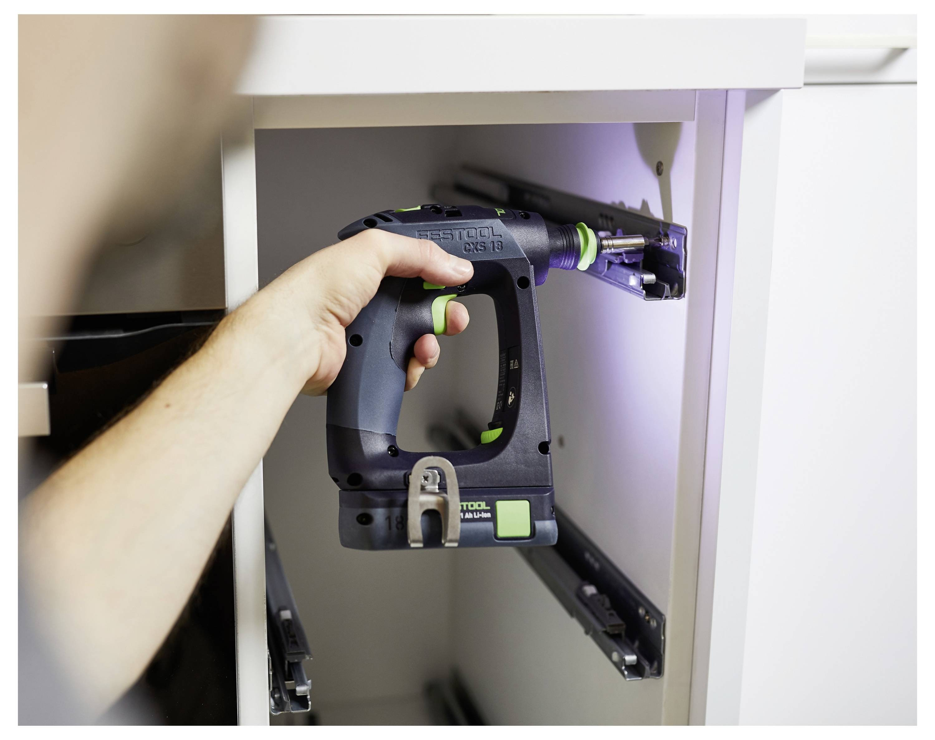 Hand, die ein Elektrowerkzeug hält, richtet Schubladenschienen in einem Holzschrank zur Installation aus.