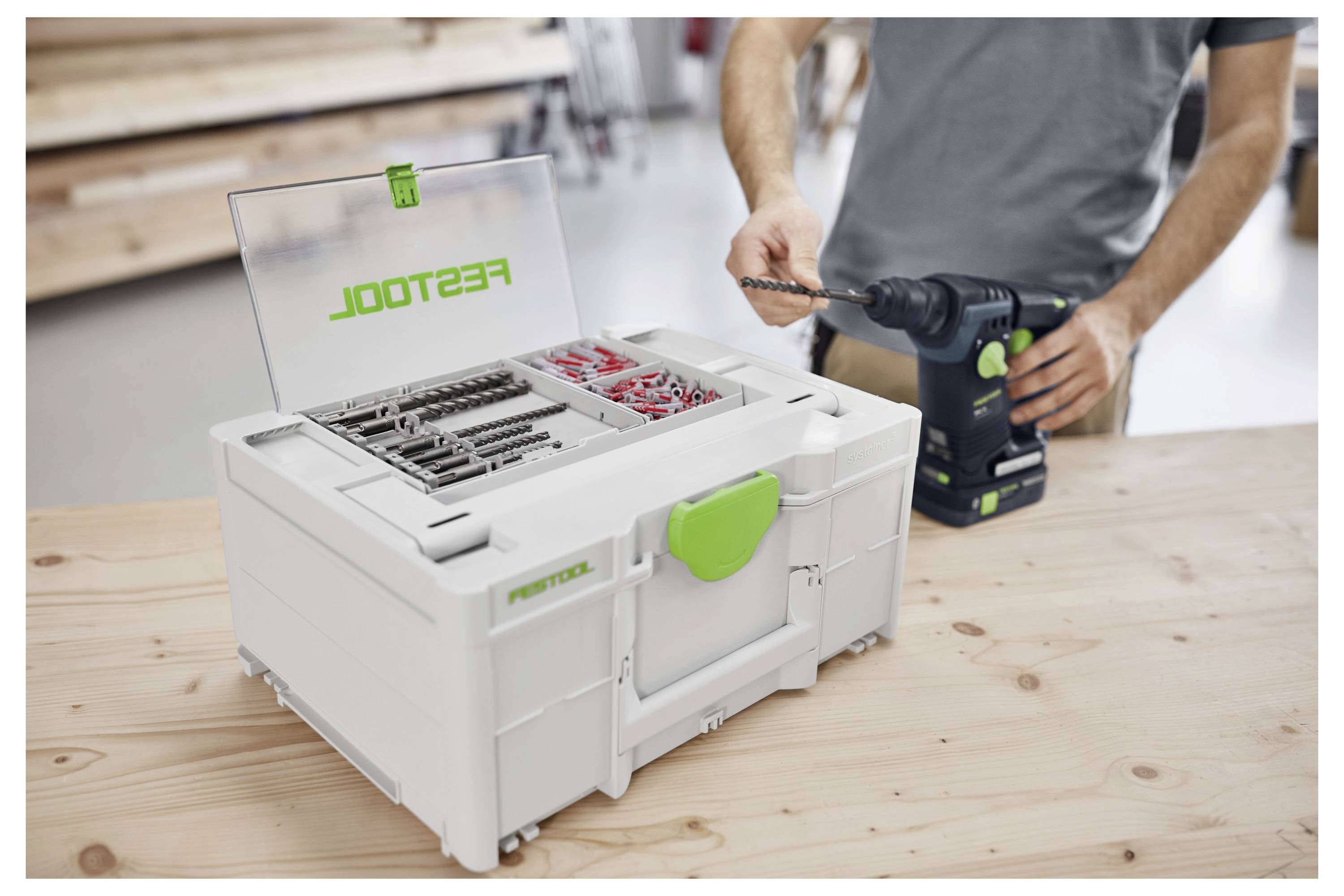 Eine Person in einer Werkstattsumgebung öffnet eine Werkzeugkiste auf einem Holztisch und untersucht ihre organisierten Fächer und Werkzeuge.