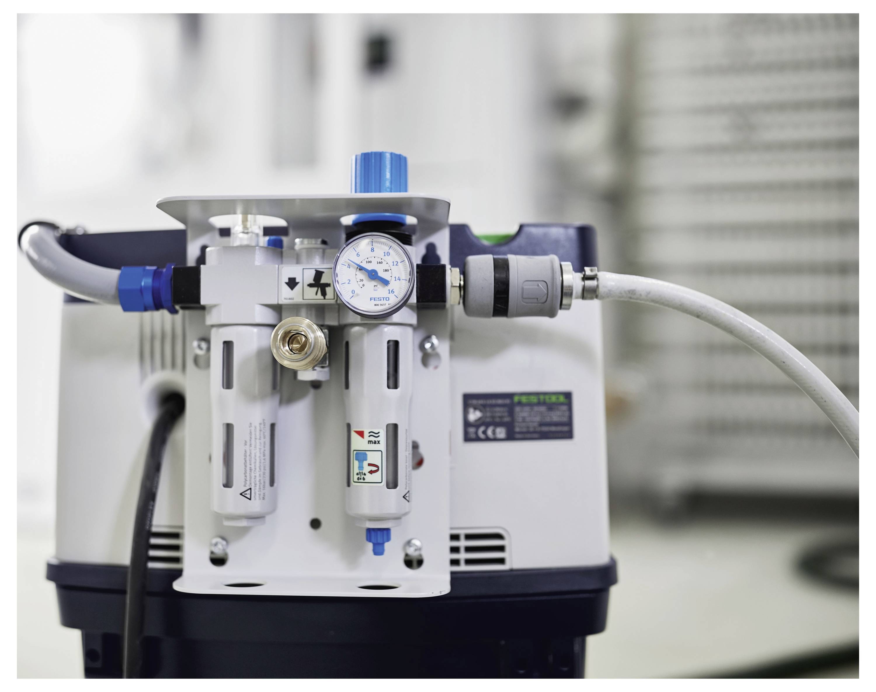 „Nahaufnahme eines Druckregulers mit Manometer, das PSI anzeigt, angebracht an einer Maschine mit Schläuchen und Verbindern.