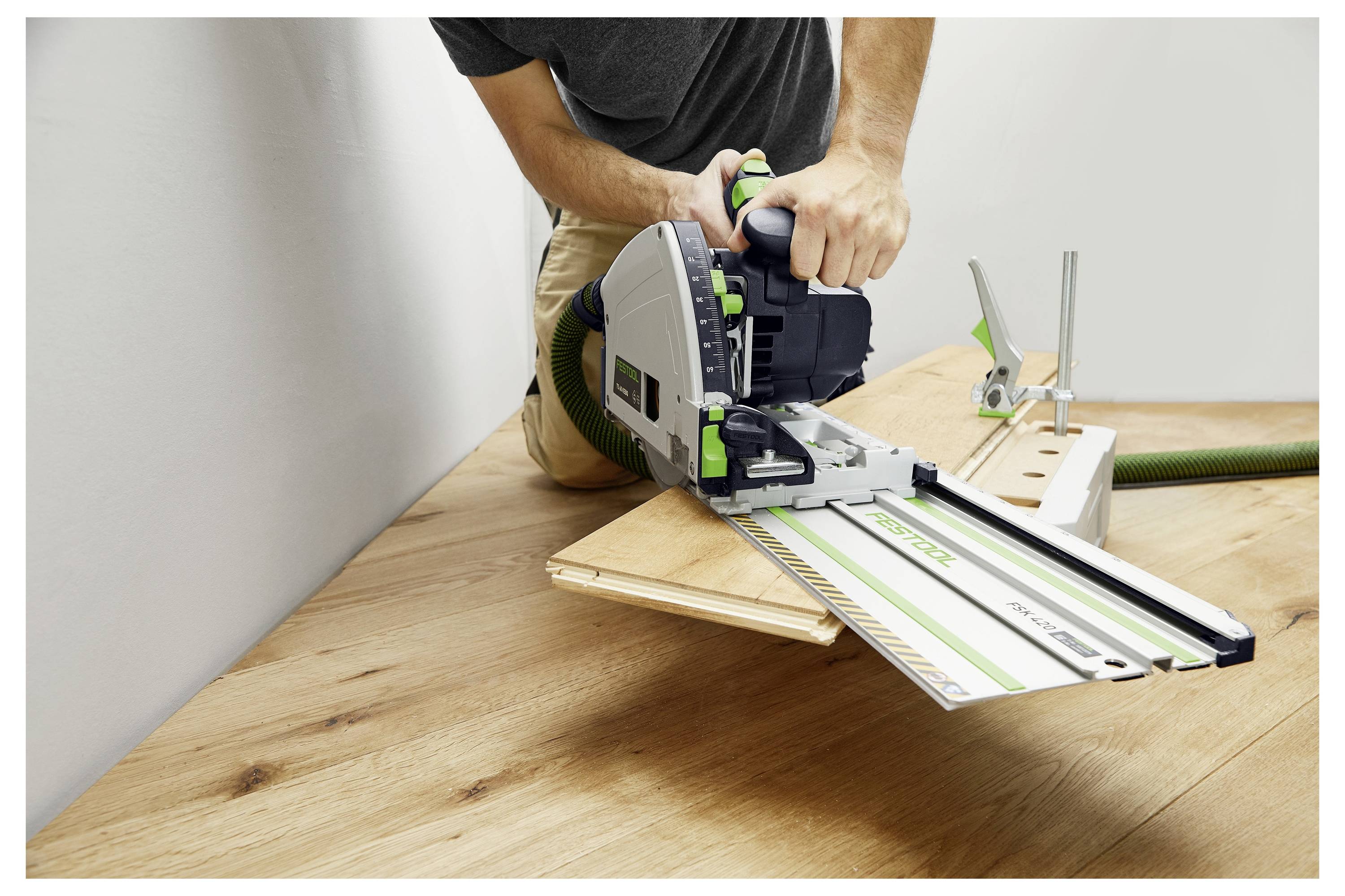 Eine Person, die eine Kreissäge mit einer Führungsschiene auf einem Holzboden benutzt, demonstriert das präzise Schneiden von Holzplatten.