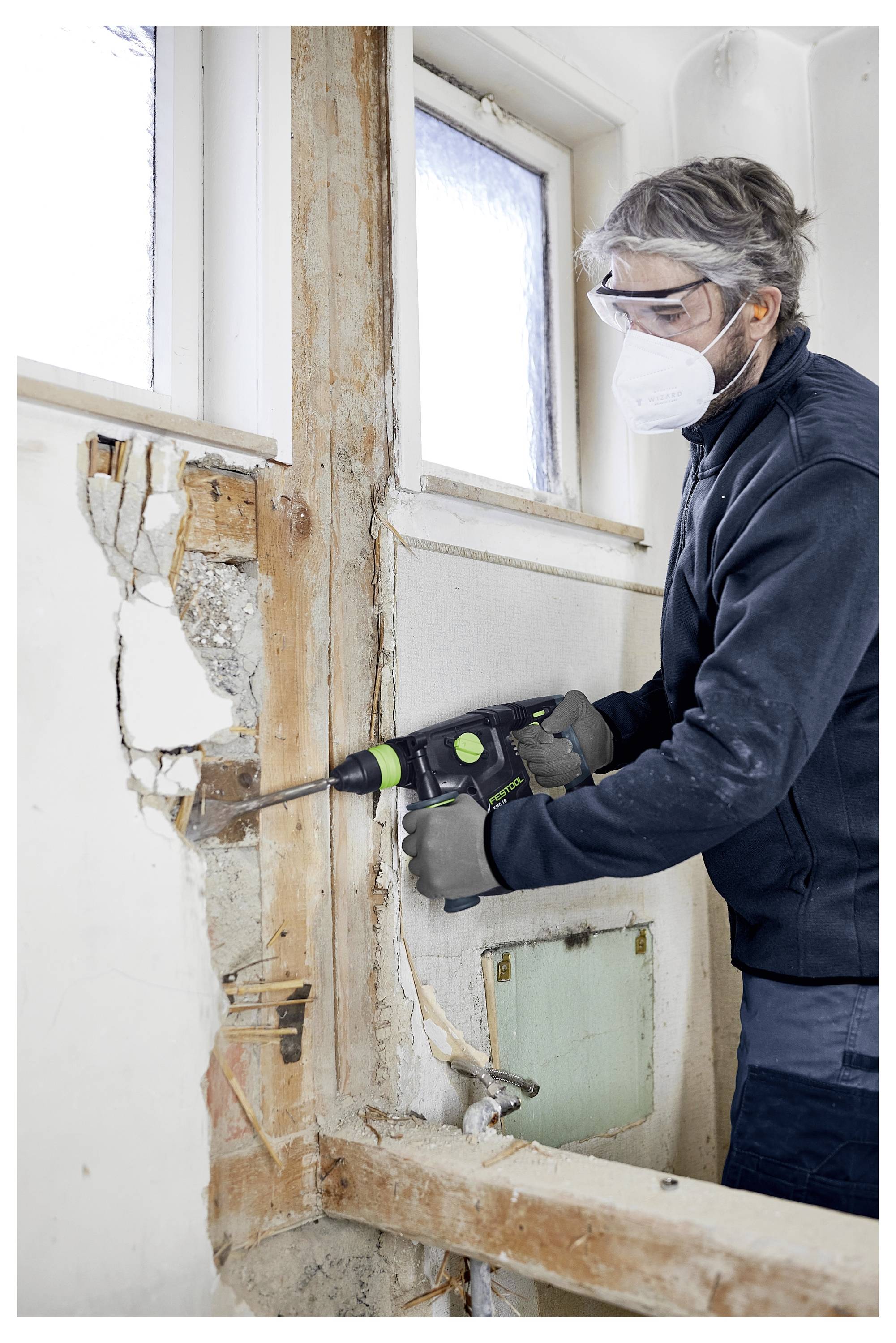 Eine Person benutzt einen Oberfräser auf einem Holzstück in einer Werkstatt und konzentriert sich auf präzise Nuten.