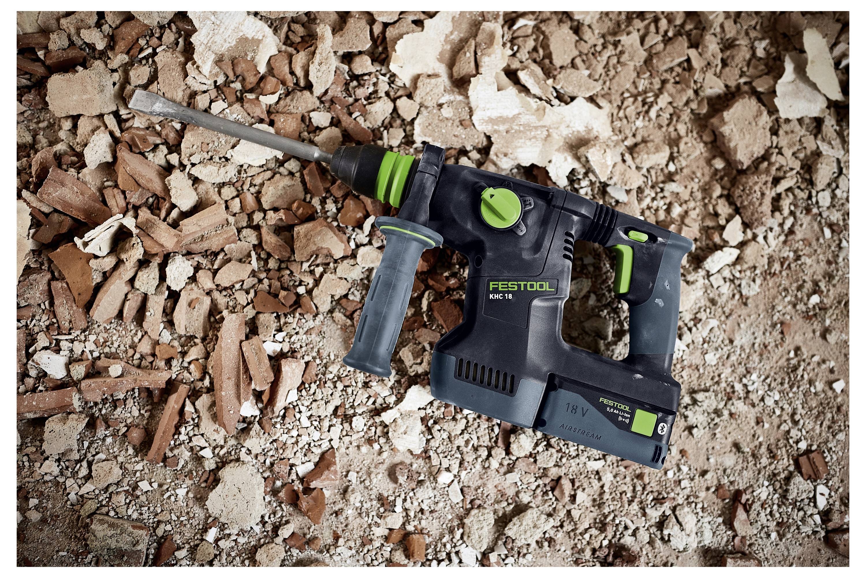 Eine Person in einem grauen Hemd hält einen kleinen, schwarzen Ohrhörer mit beiden Händen in einem hellen Raum.