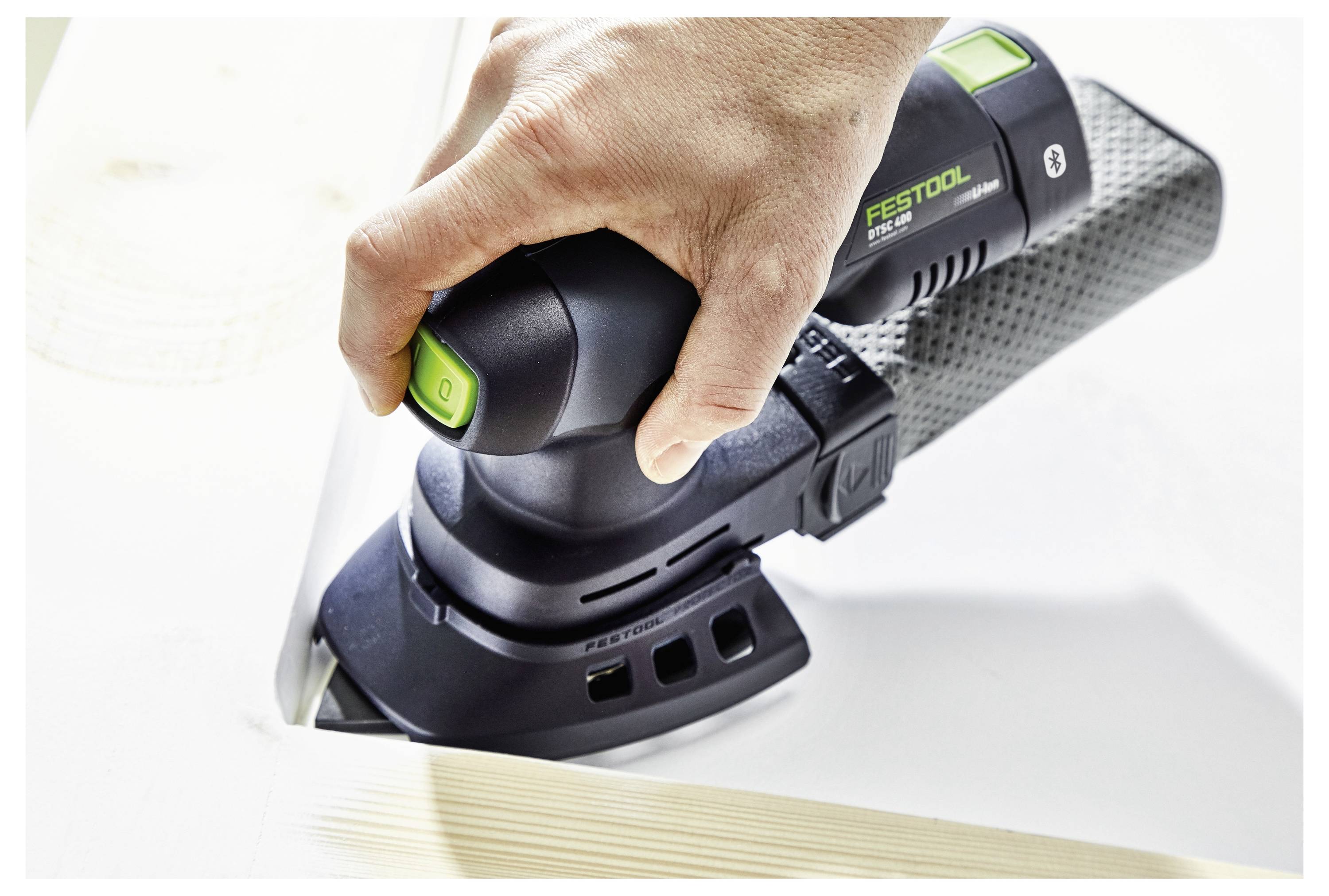 A person uses a handheld Festool sander on a wooden surface, smoothing a corner, emphasizing precision in woodworking tasks.