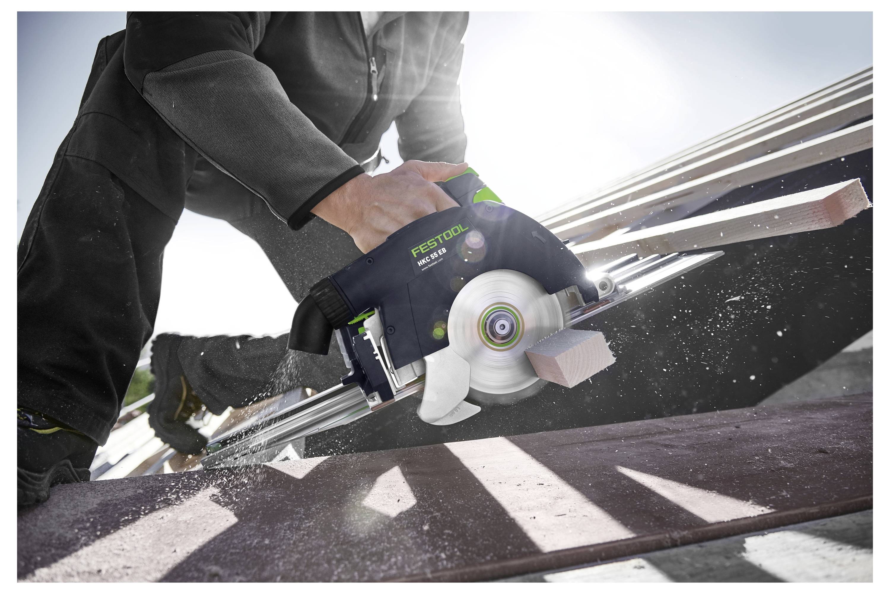 Eine Person, die eine Festool-Kreissäge verwendet, um Holzbalken auf einem Dach durchzusägen, mit Sonnenlicht, das im Hintergrund scheint.