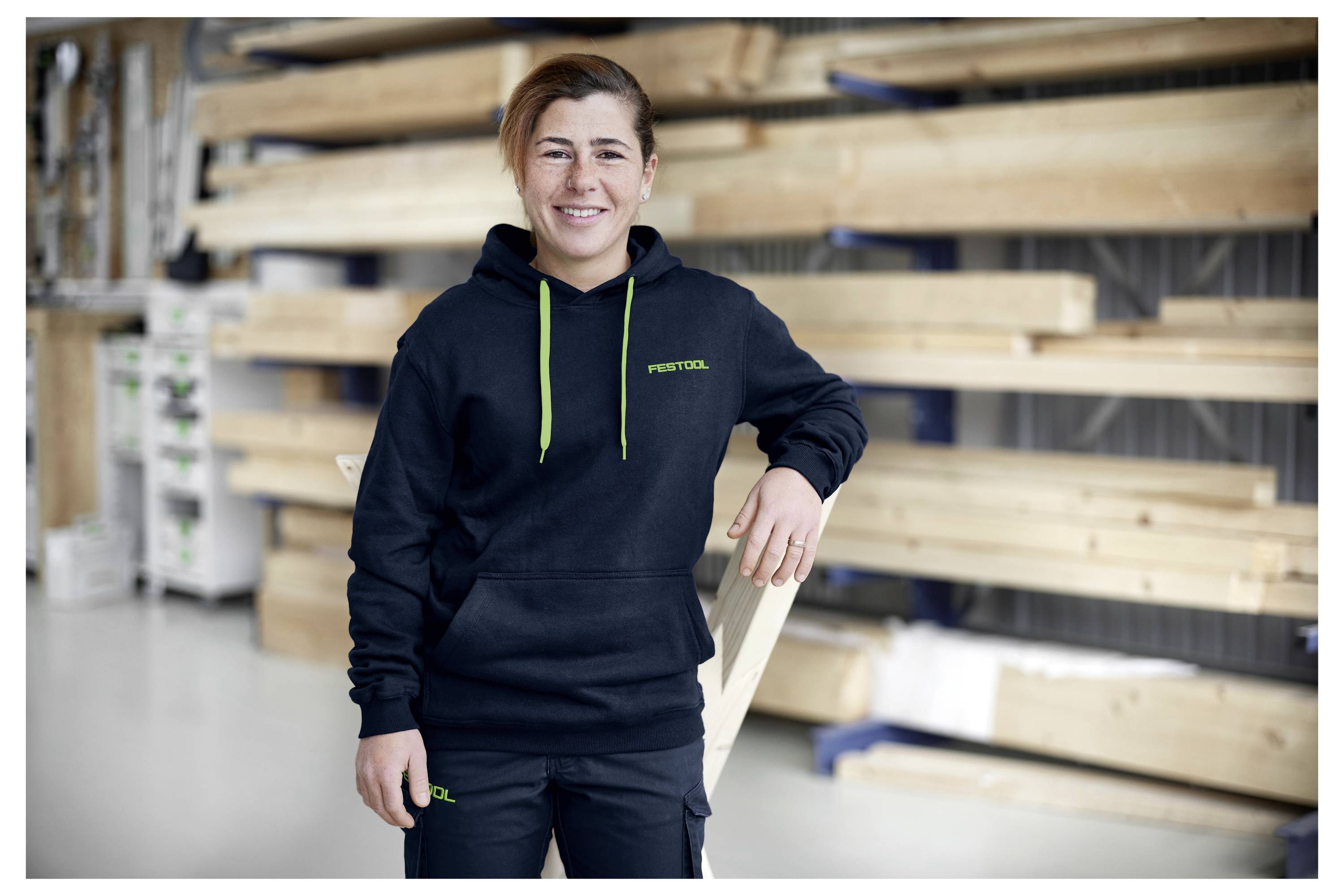 „Eine Person in einer Werkstatt lehnt sich auf einen Stuhl, trägt einen schwarzen Hoodie mit dem Logo „Festool