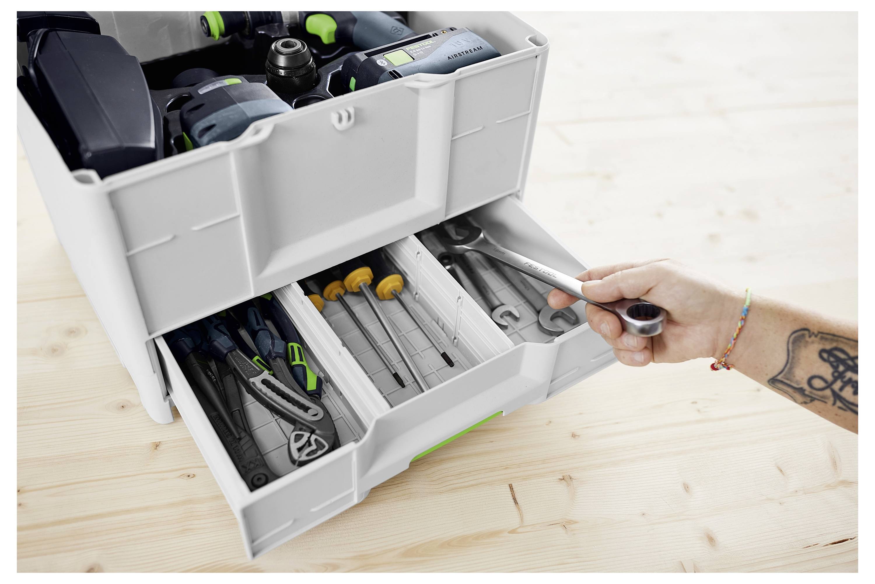 Eine Person bedient ein Elektrowerkzeug mit einem grün-schwarzen Griff auf einem Schienensystem, vermutlich zum präzisen Schneiden auf einer Oberfläche.