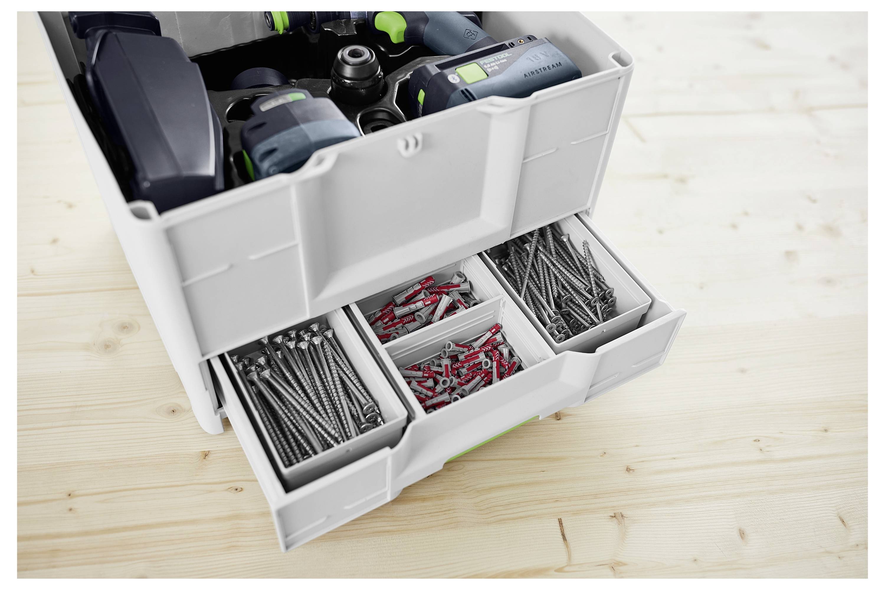 Ein Satz von Werkzeugen in einem weißen Schubladensystem auf einer Holzoberfläche. Die obere Schublade enthält Elektrowerkzeuge, während die unteren Schubladen Schrauben und Bohrer enthalten.