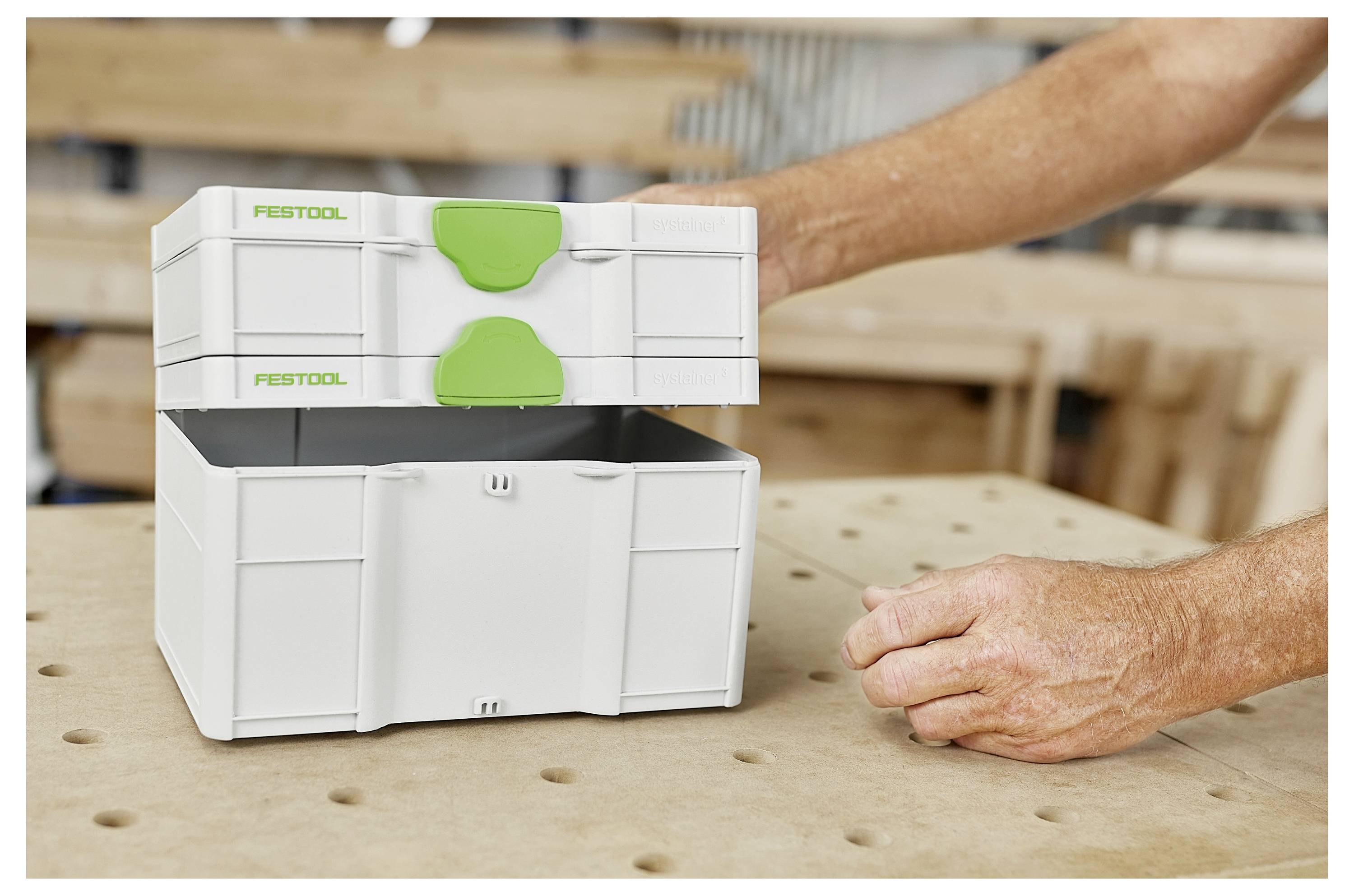 Eine Person kniet auf einem Hartholzboden und bedient einen professionellen Reinigungsstaubsauger, der an einem großen Schlauch angebracht ist, und zielt auf einen Teppichbereich.