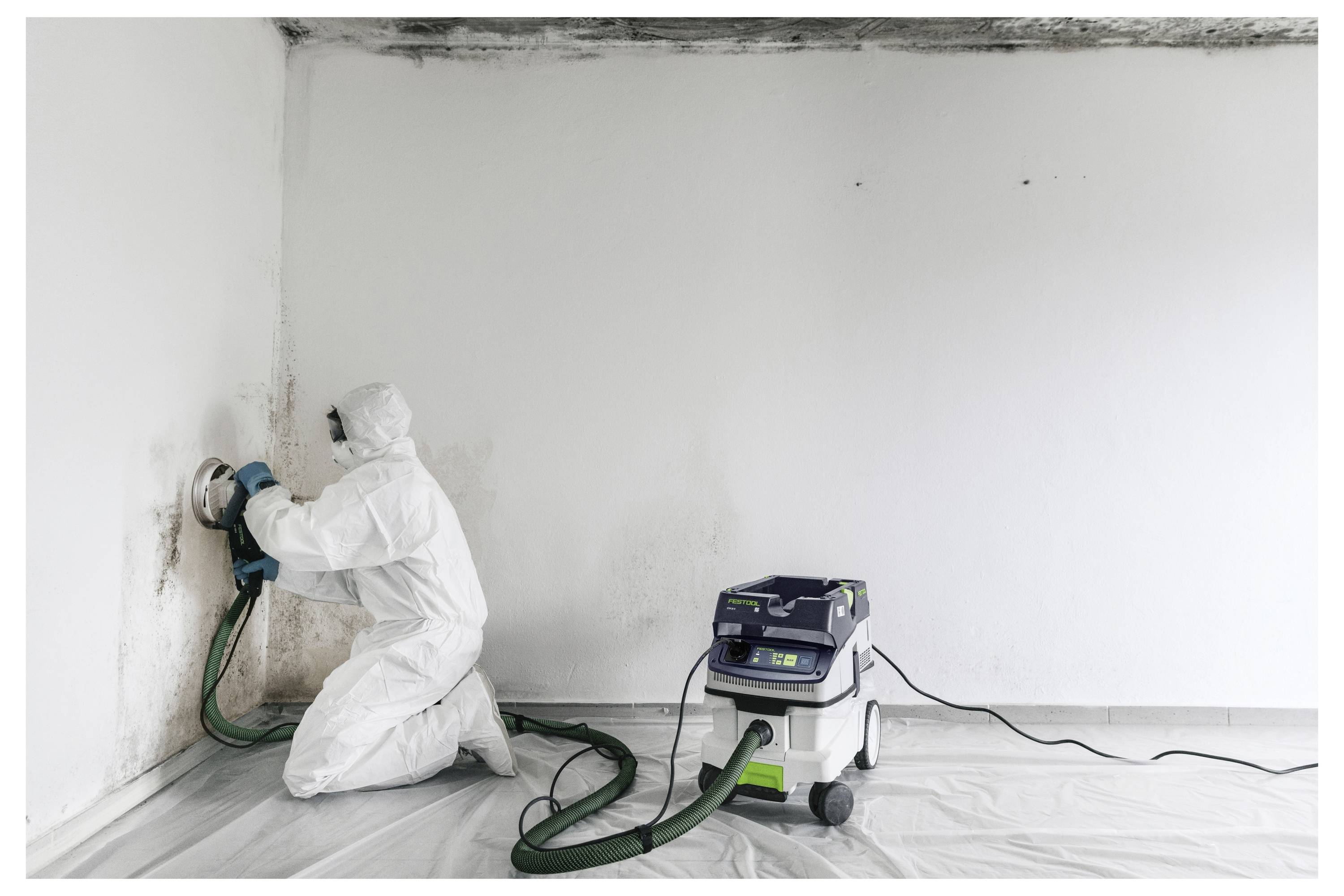 Eine Person trägt eine weiße Werkzeugkiste eine Treppe in einem teilweise renovierten Raum hinauf.