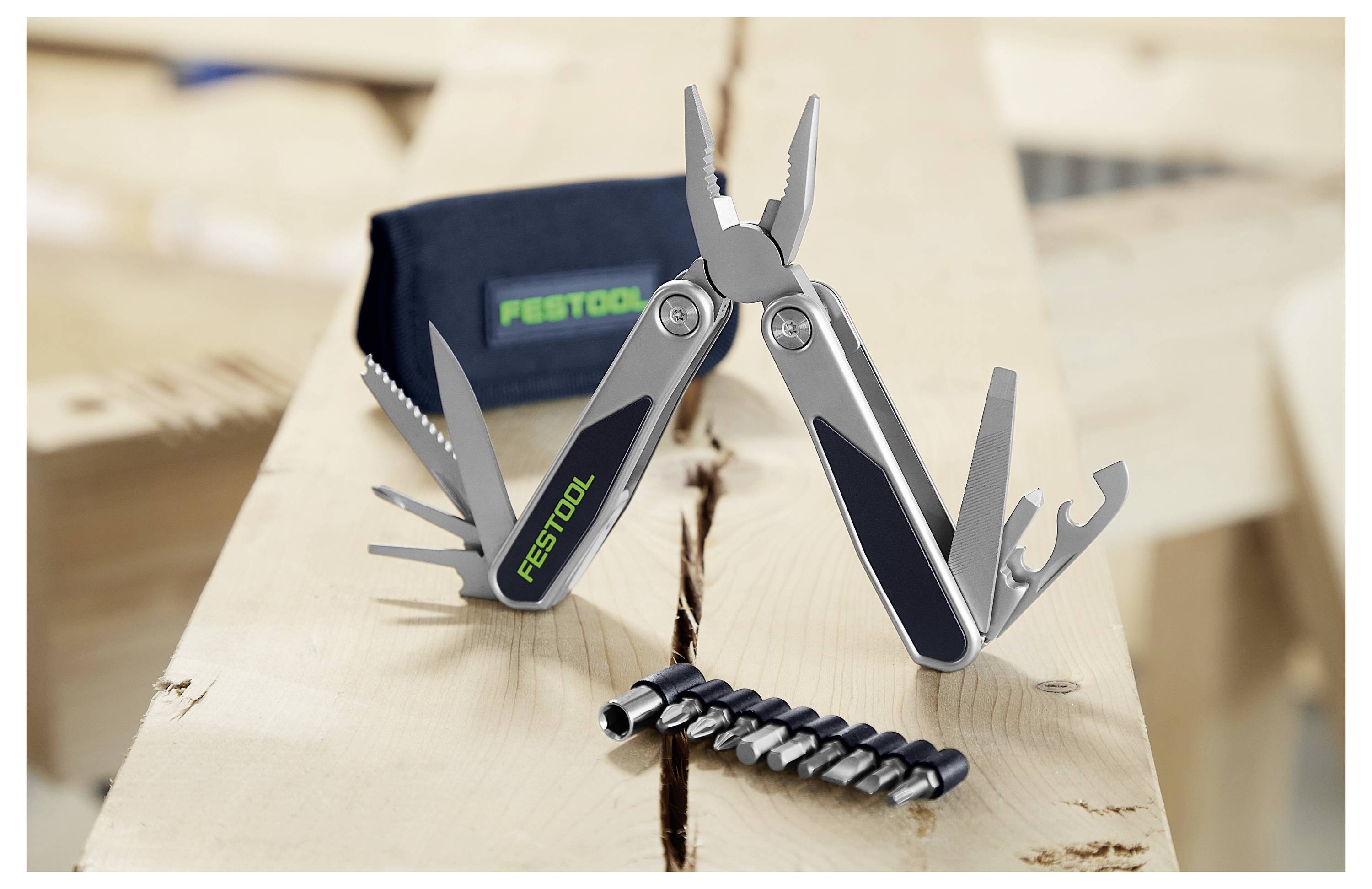 Ein silbernes Multitool mit verschiedenen ausklappbaren Werkzeugen, darunter Zangen und Schraubendreher, auf einer Holzoberfläche; das Logo „Festool