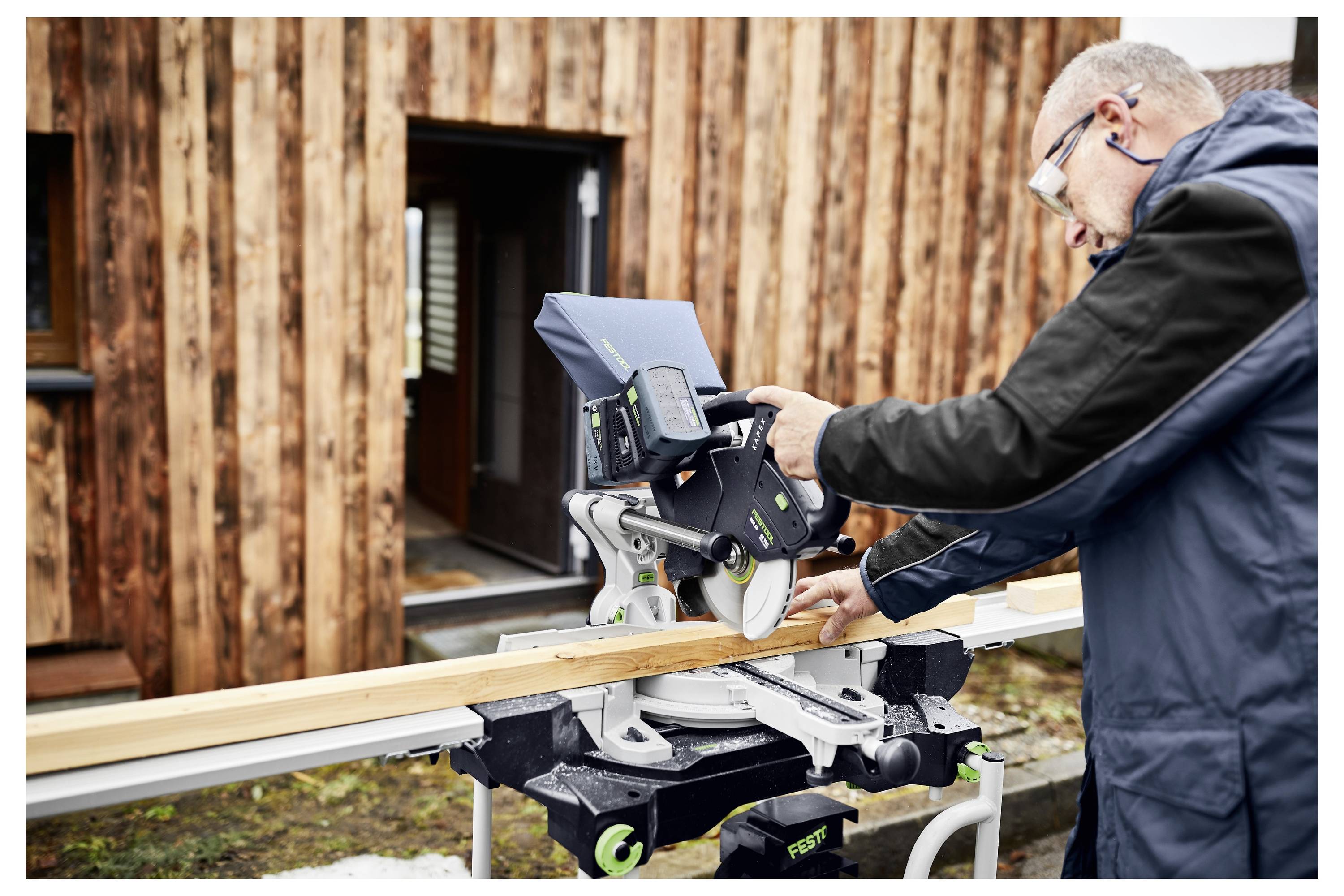 Eine Person, die einen Festool-Staubabsauger eine Holztreppe hinauträgt, zeigt die Portabilität und Benutzerfreundlichkeit für Reinigungsaufgaben.