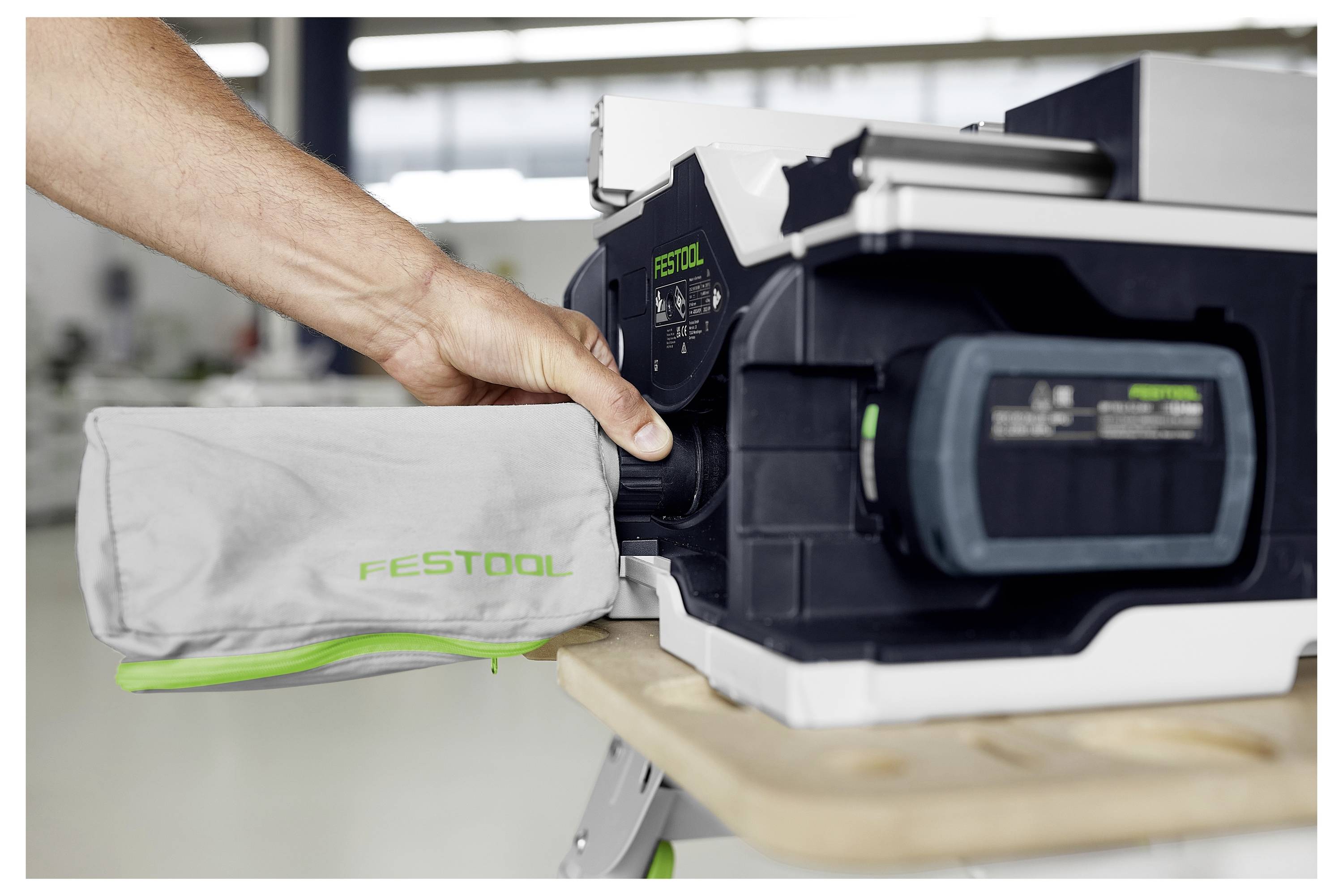 Eine Person befestigt einen Staubsack an einem Festool-Elektrowerkzeug auf einer Werkbank in einer Werkstatt.