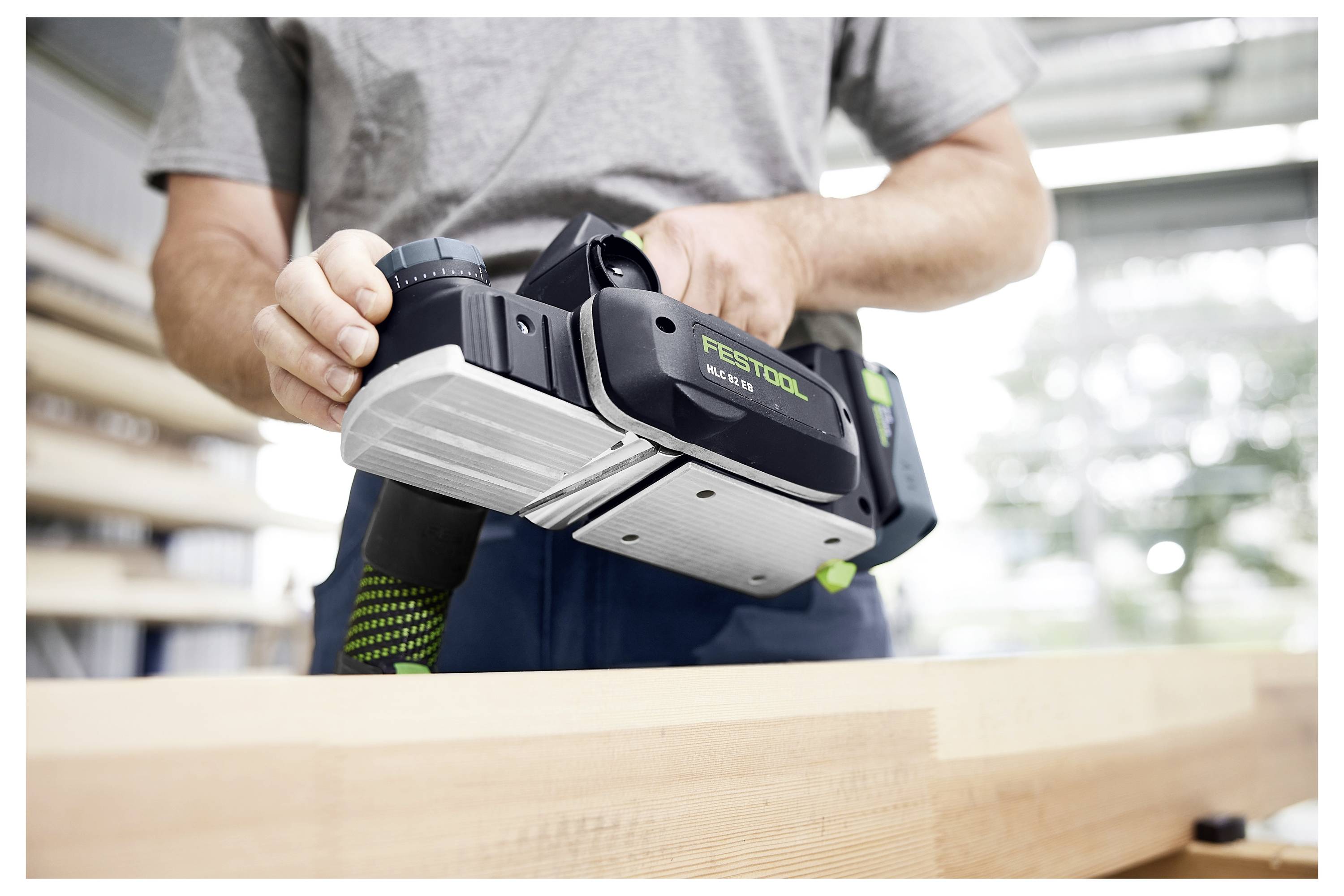 Eine Person benutzt einen Festool-Hobel auf einer Holzoberfläche und trägt ein graues Hemd. Der Fokus liegt auf dem Werkzeug und der Holzbearbeitung.