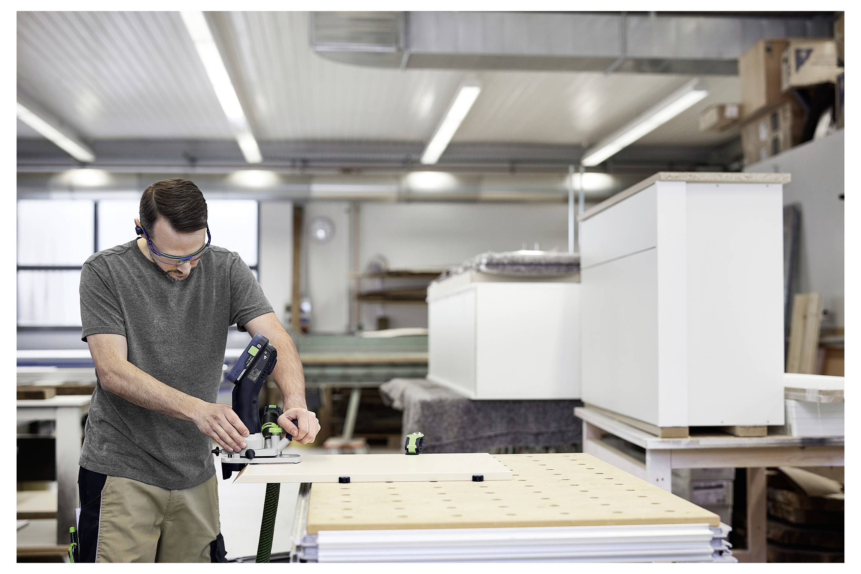 Eine Person mit Tätowierungen und Armbändern hält blaue und schwarze Schleifpapierblätter mit Löchern an einem Arbeitsplatz.