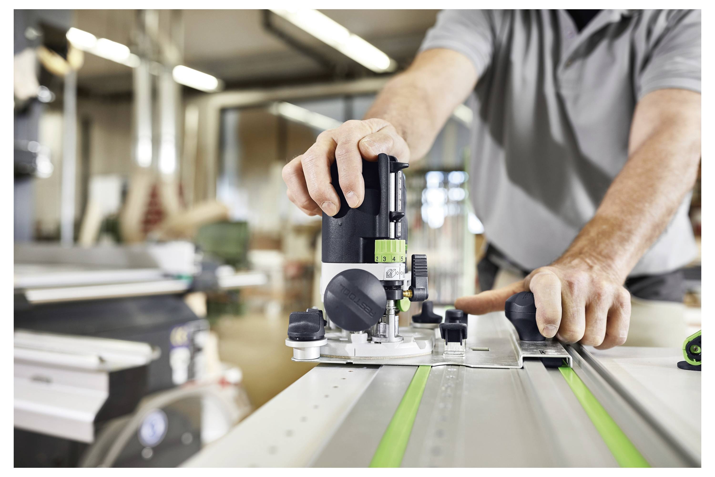 A person operates a woodworking router, guiding it along a track in a workshop, focusing on precision and detail in craftsmanship.