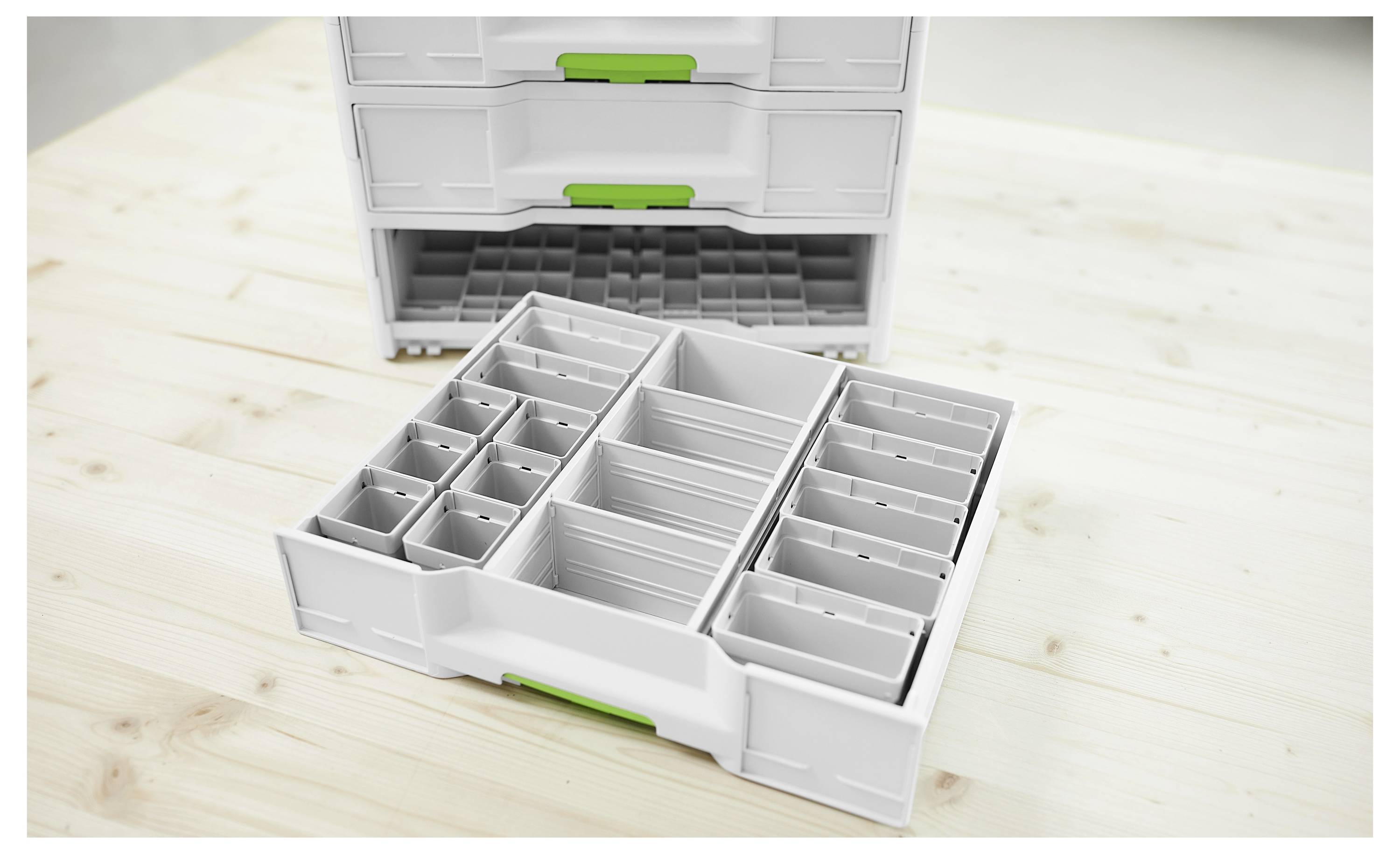 Gestapelte weiße Lagerkisten mit grünen Griffen, mit einem abnehmbaren Tablett mit verstellbaren Fächern, auf einer Holzoberfläche platziert.