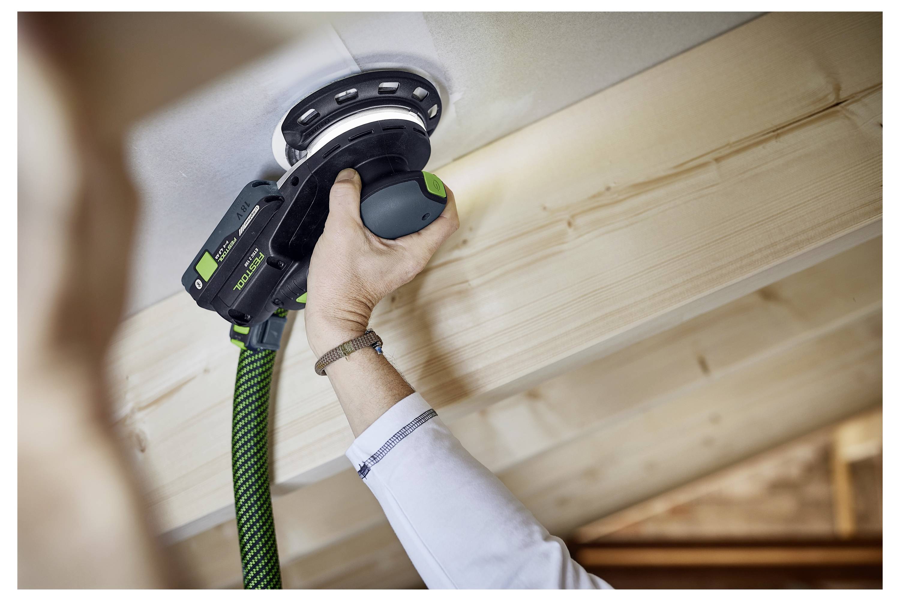 Eine Person schleifte einen Holzbalken mit einem Elektroschlifer und hebt dabei Heimrenovierung oder Holzbearbeitung in einer Werkstattumgebung hervor.