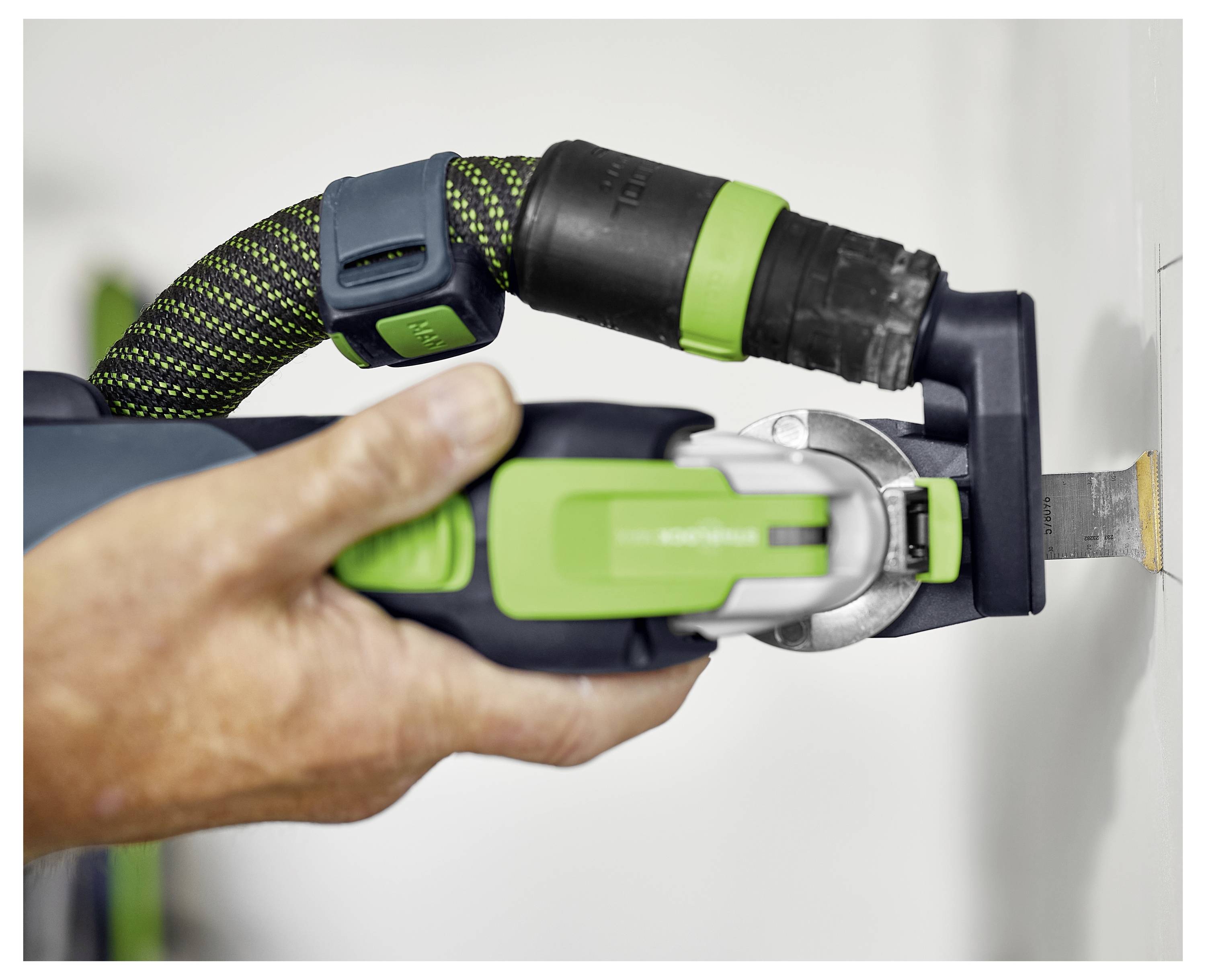 Eine Person verwendet ein grünes und schwarzes Elektrowerkzeug, um präzise in eine Wand zu schneiden und demonstriert damit präzise, kontrollierte Schneidfunktionalität.