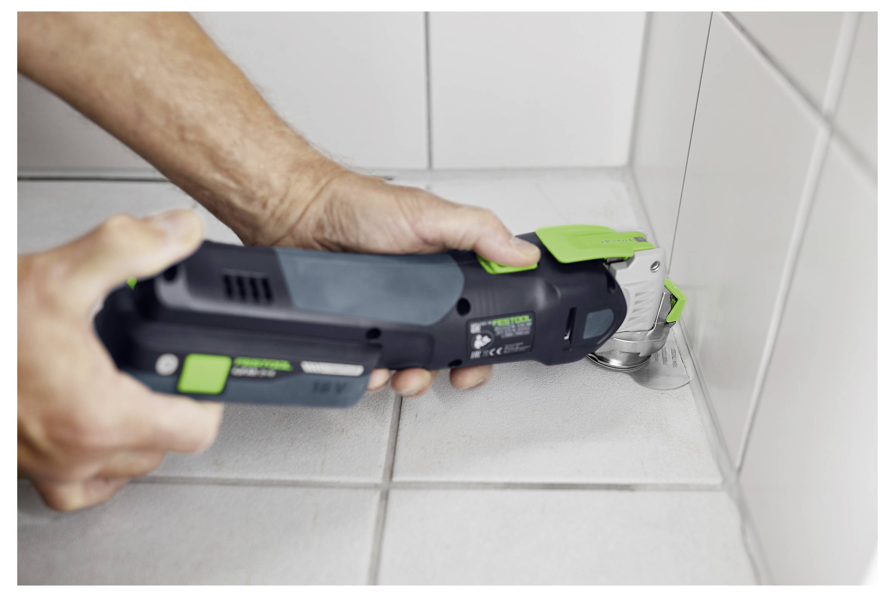 Eine Person benutzt ein Elektrowerkzeug, um Fliesen an der Ecke eines gefliesten Bodens zu schneiden, was Heimwerker- oder Renovierungsarbeiten veranschaulicht.