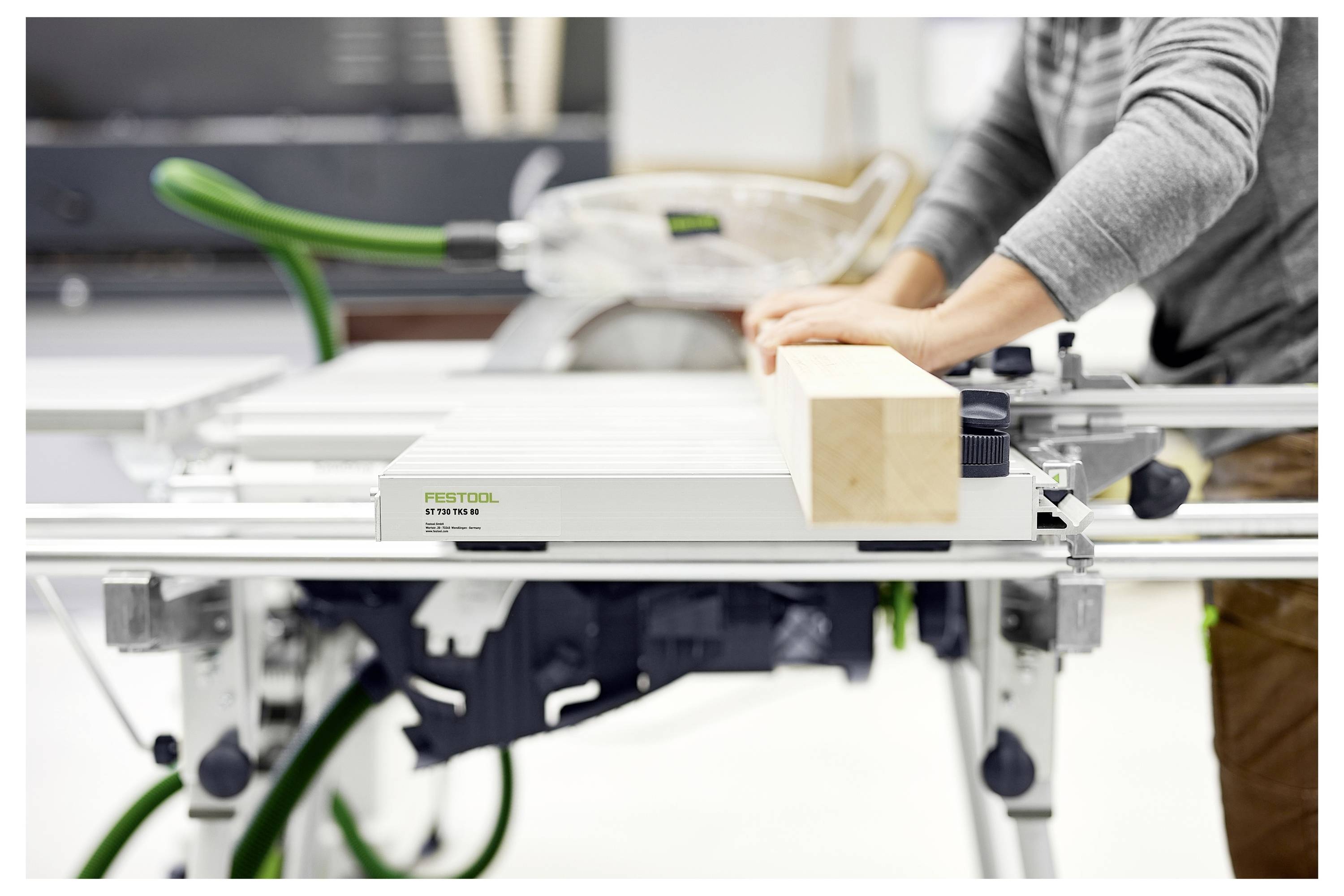 Person, die eine Schiebtischsäge verwendet, um einen Holzbalken zu schneiden, zeigt präzise Handhabung von Holzbearbeitungswerkzeugen in einer Werkstattsituation.