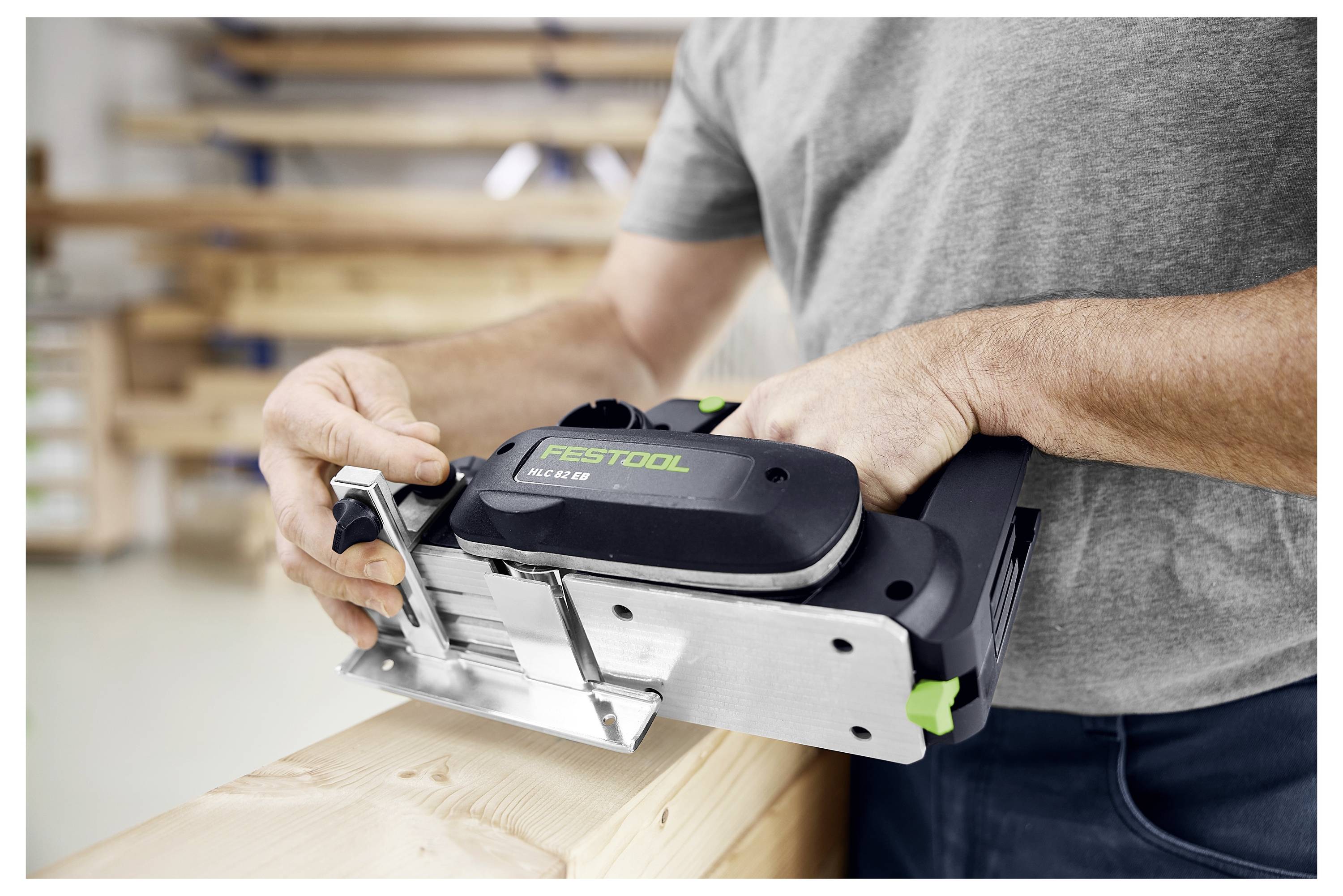 Eine Person verwendet einen elektrischen Handhobel, um eine Holzplanke in einer Werkstattumgebung zu glätten.