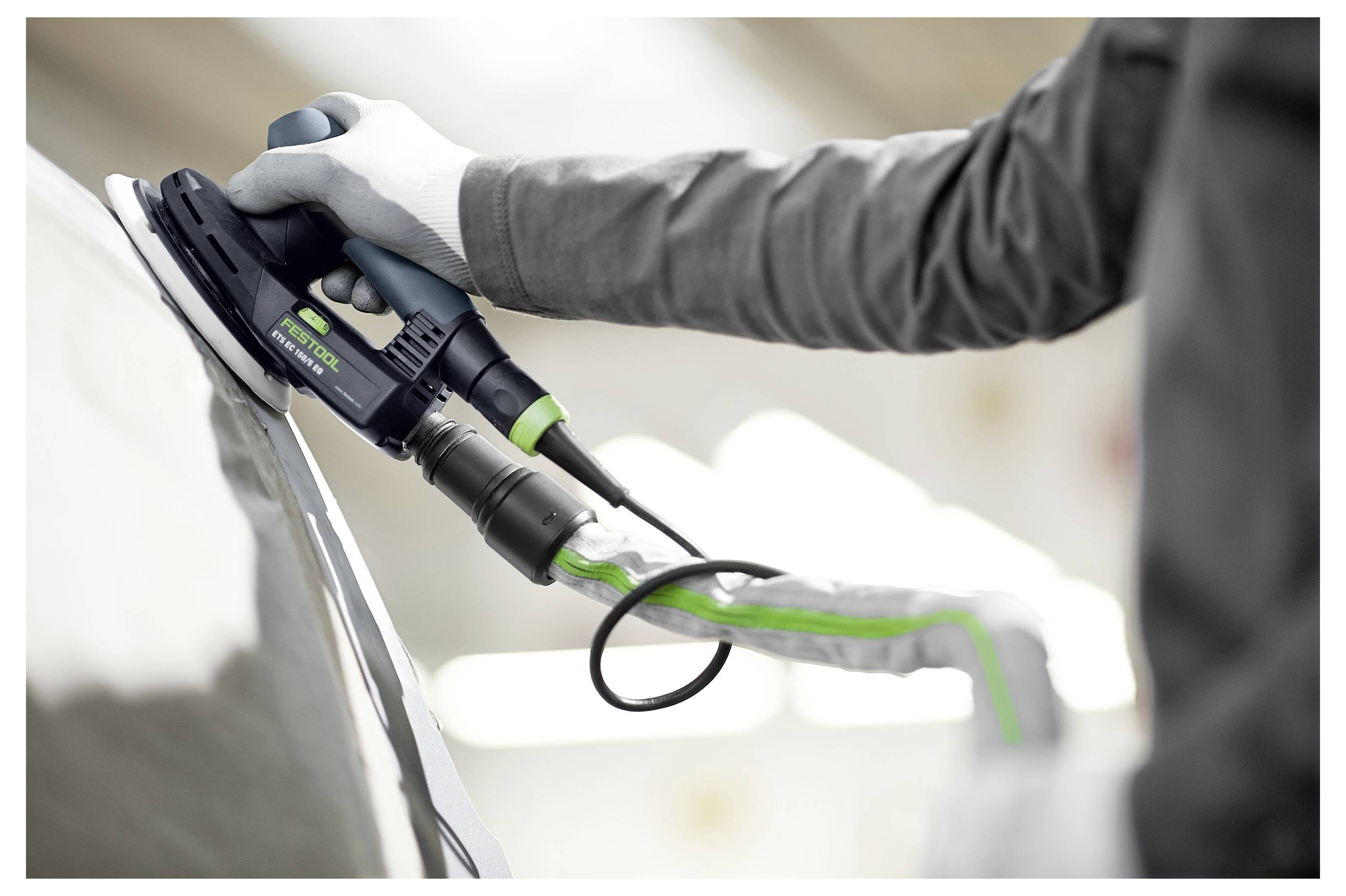 Eine Person mit Handschuhen nutzt ein Elektrowerkzeug, um die Oberfläche eines Autos zu polieren und konzentriert sich dabei auf einen reflektierenden, glatten Glanz.