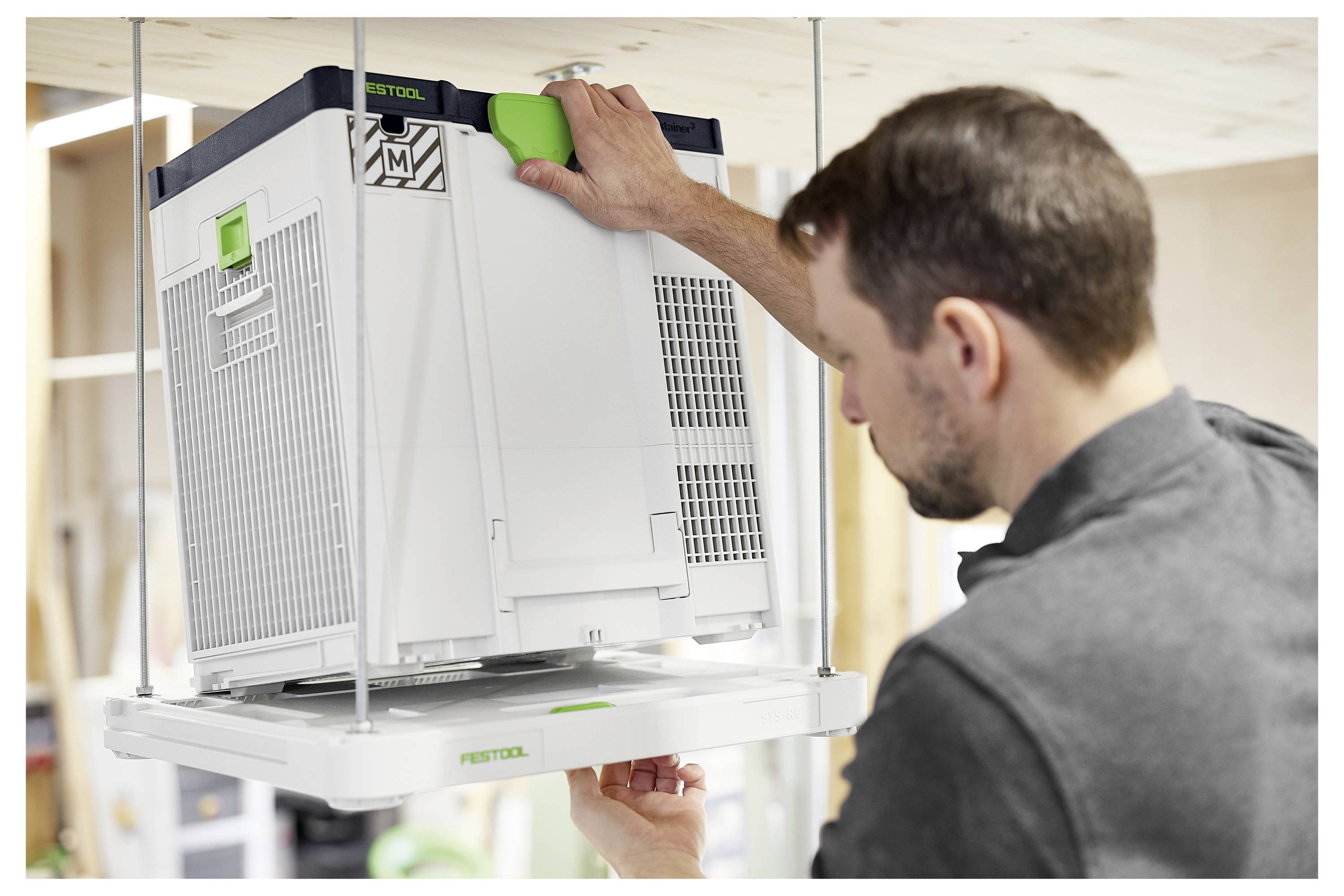 Ein Arbeiter kniet nieder, während er ein Elektrowerkzeug verwendet, das mit einem großen Vakuumsystem auf einer Baustelle verbunden ist, was auf einen Fokus auf Sicherheit und Sauberkeit hindeutet.