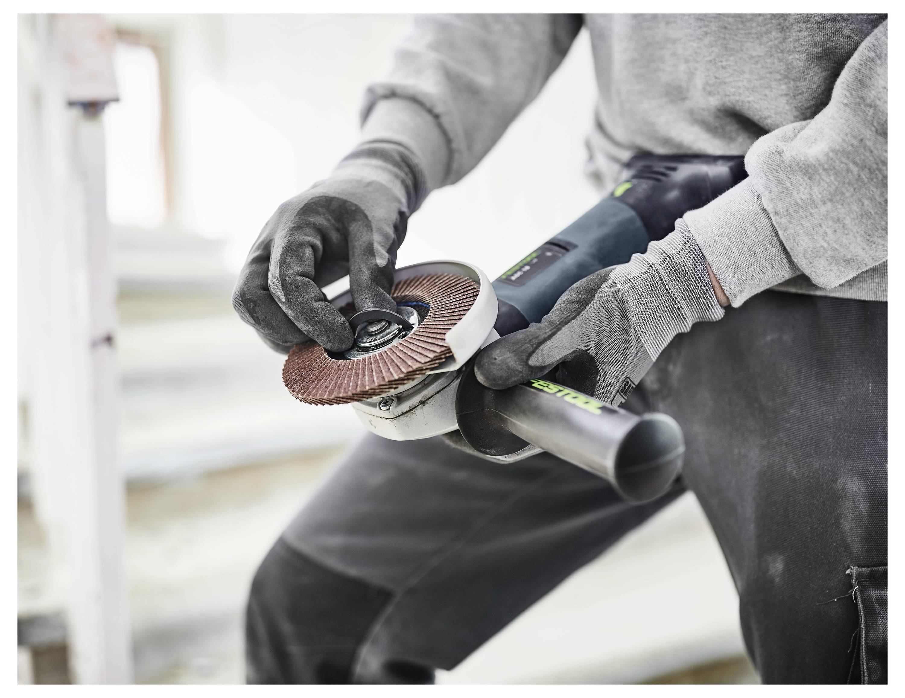 Eine Person, die Handschuhe trägt, nutzt einen Winkelschleifer auf einer Baustelle und konzentriert sich dabei auf die Einstellung des Werkzeugs.