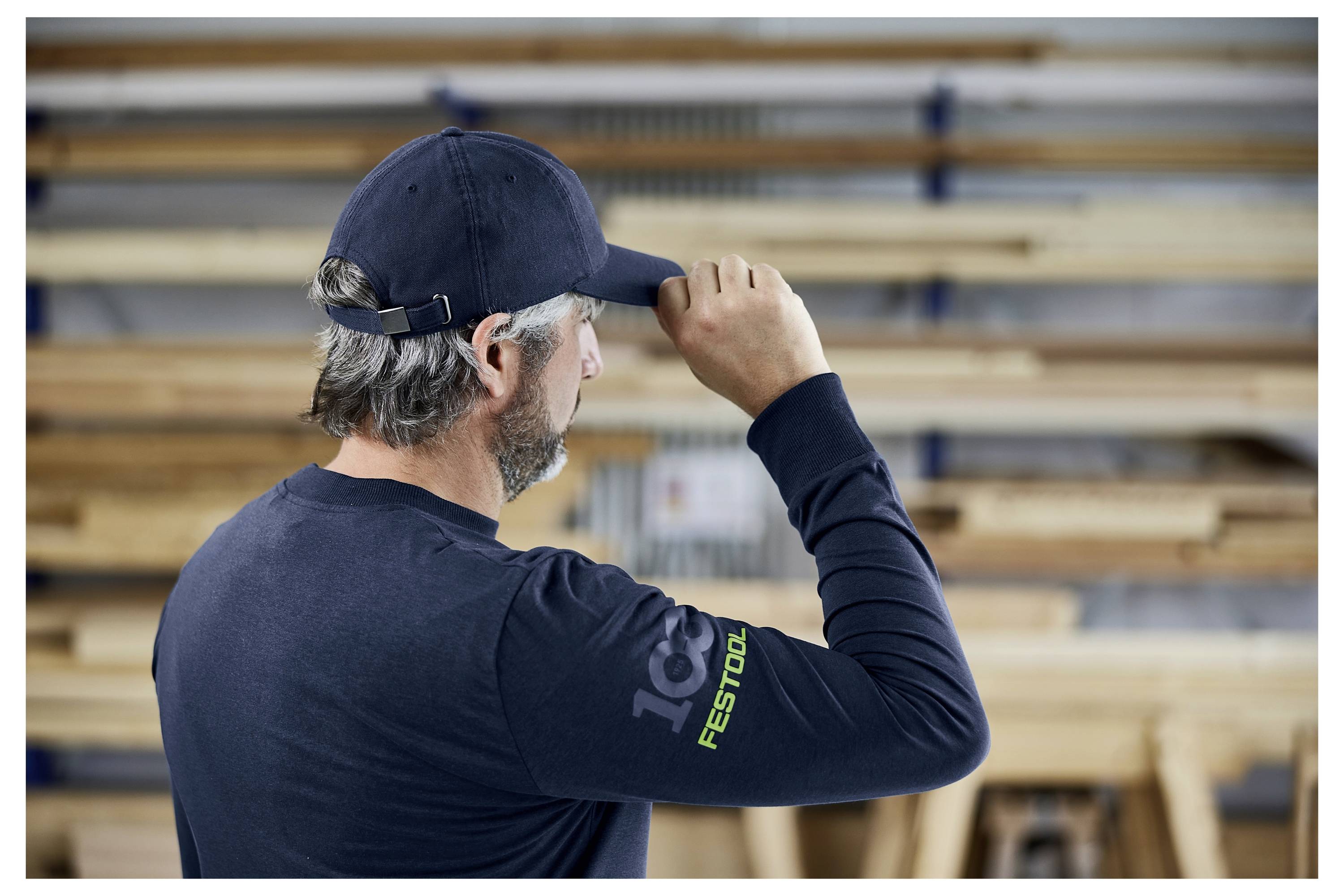 Ein Mann benutzt ein Schleifdrehzeug an einem weißen Schrank, trägt ein graues Hemd und Gehörschutz in einer Werkstattsituation.