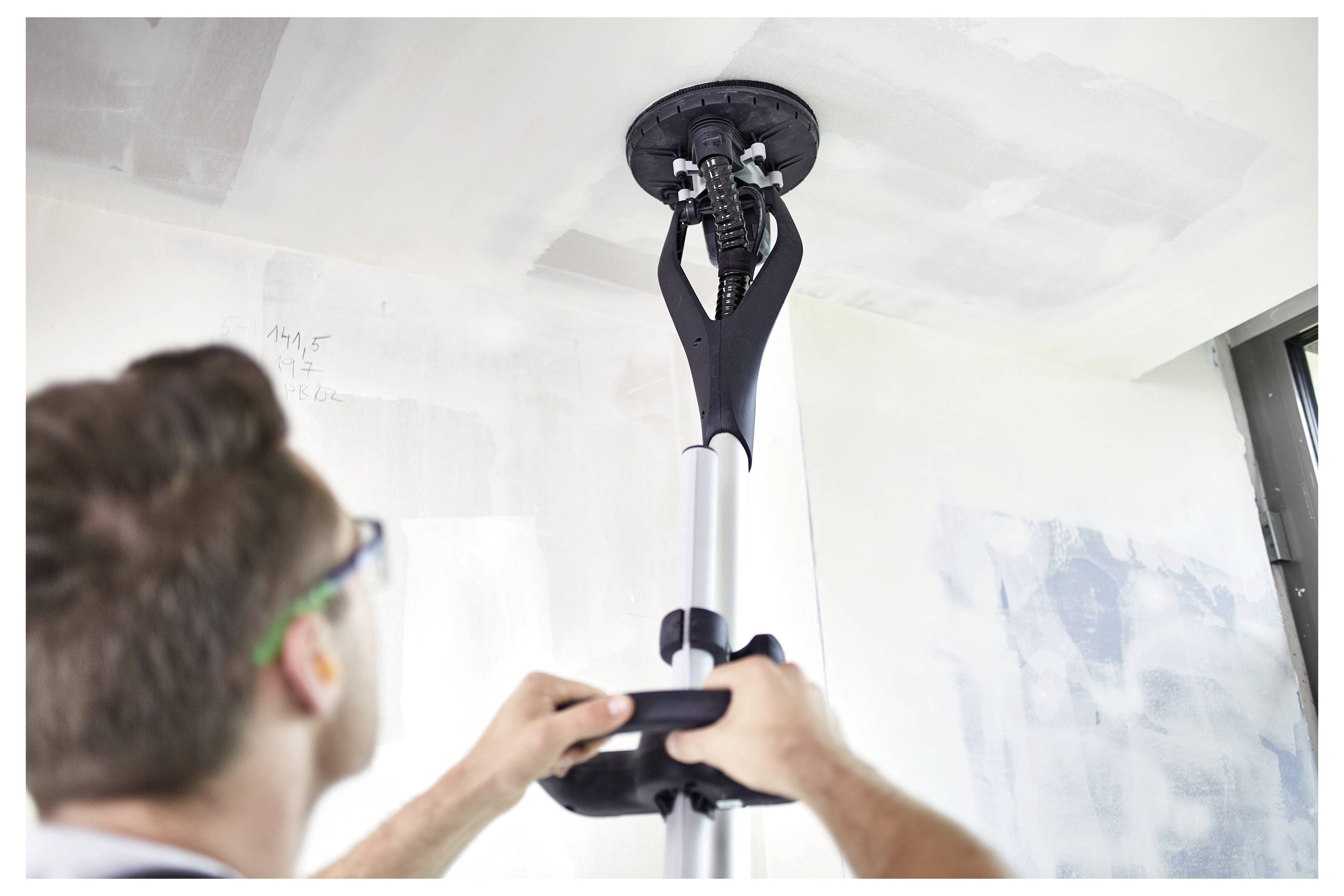 Eine Person verwendet ein Deckenschleifgerät auf einer teilweise verputzten Decke und konzentriert sich darauf, die Oberfläche zu glätten.