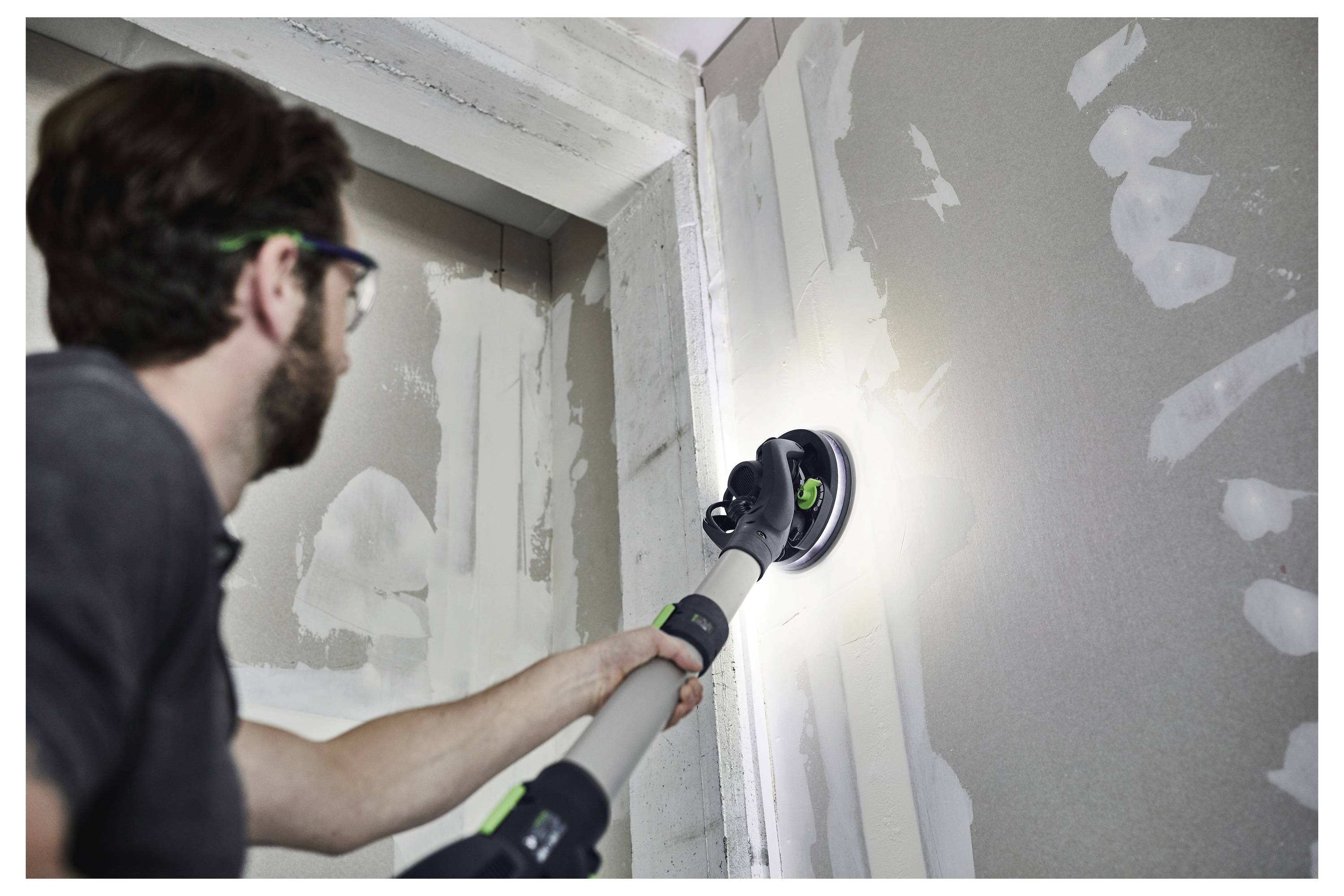 Eine Person mit einem Werkzeuggürtel bedient einen tragbaren Elektroschleifen mit einem blauen Schleifteller, was die Verwendung in einem Holzbearbeitungs- oder Baustellen-Setting veranschaulicht.