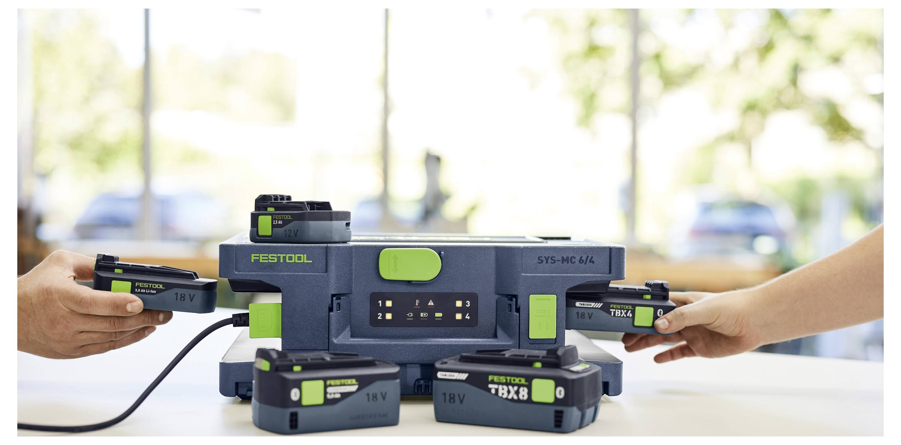 Person kniet auf einem Baustellenboden und öffnet eine graue Werkzeugkiste. Wände sind unvollständig, mit sichtbarem Trockenbau.