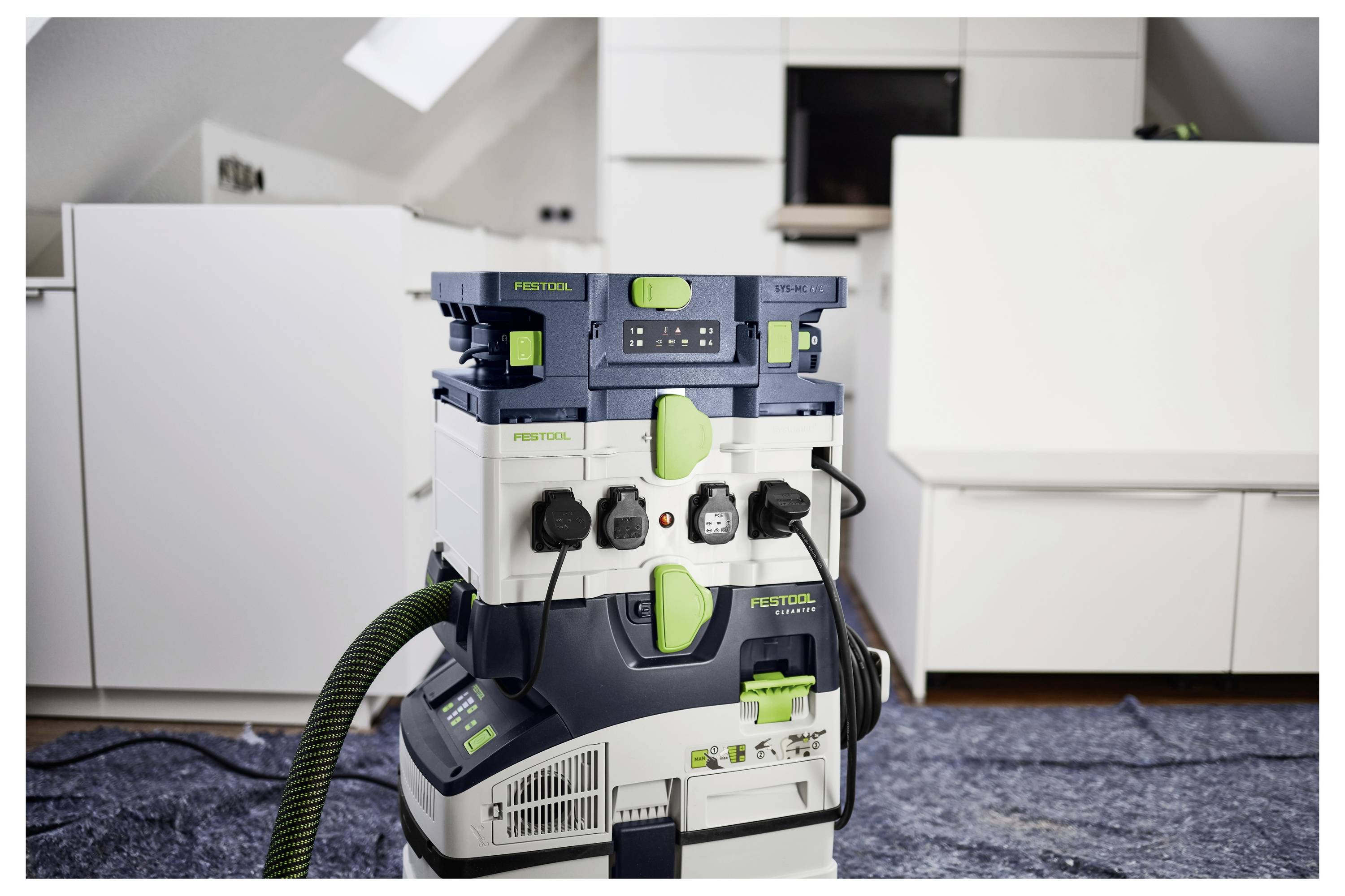 Ein Festool-Staubsauger steht auf einer blauen Plane in einer modernen, weiß eingerichteten Küche, umgeben von Arbeitsplatten und minimalistischer Dekoration.