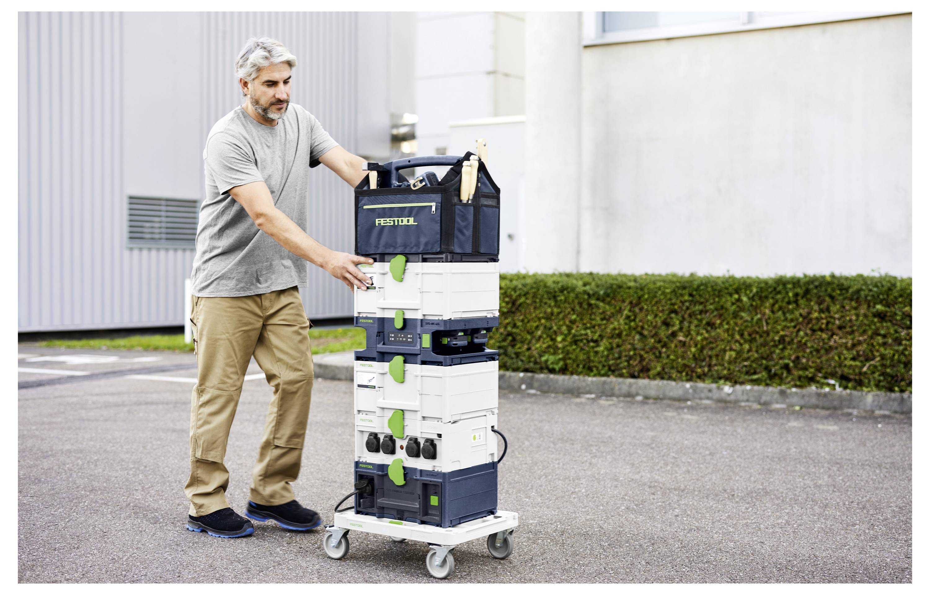 Eine Person schiebt einen Stapel von Festool-Ausrüstung auf einem Handwagen nach draußen. Die Ausrüstung ist in modularen Behältern organisiert.