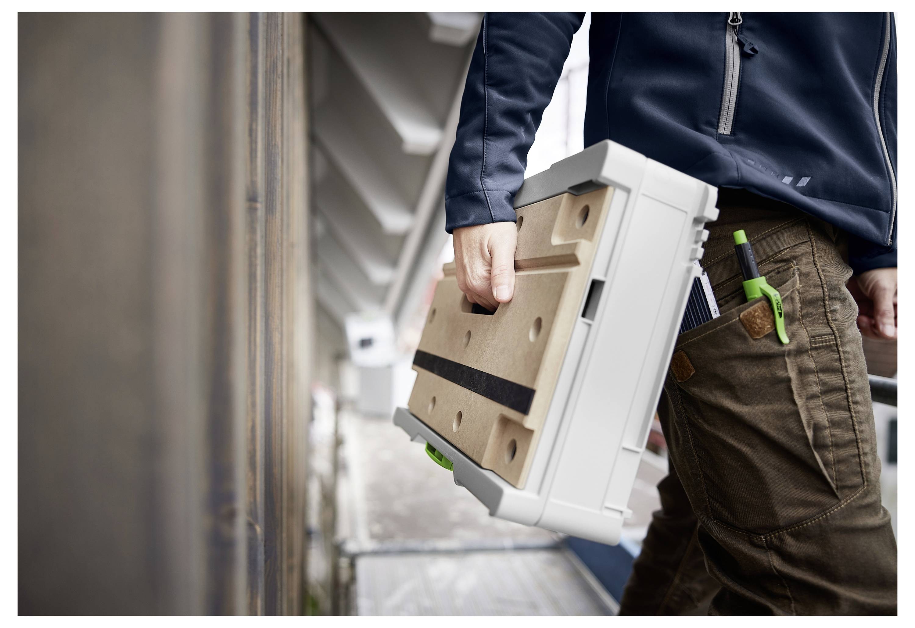 Eine Person, die eine Schutzbrille trägt, bedient ein Elektrowerkzeug in einer Werkstatt, die mit Holzmöbeln und Schränken in der Bauphase gefüllt ist.