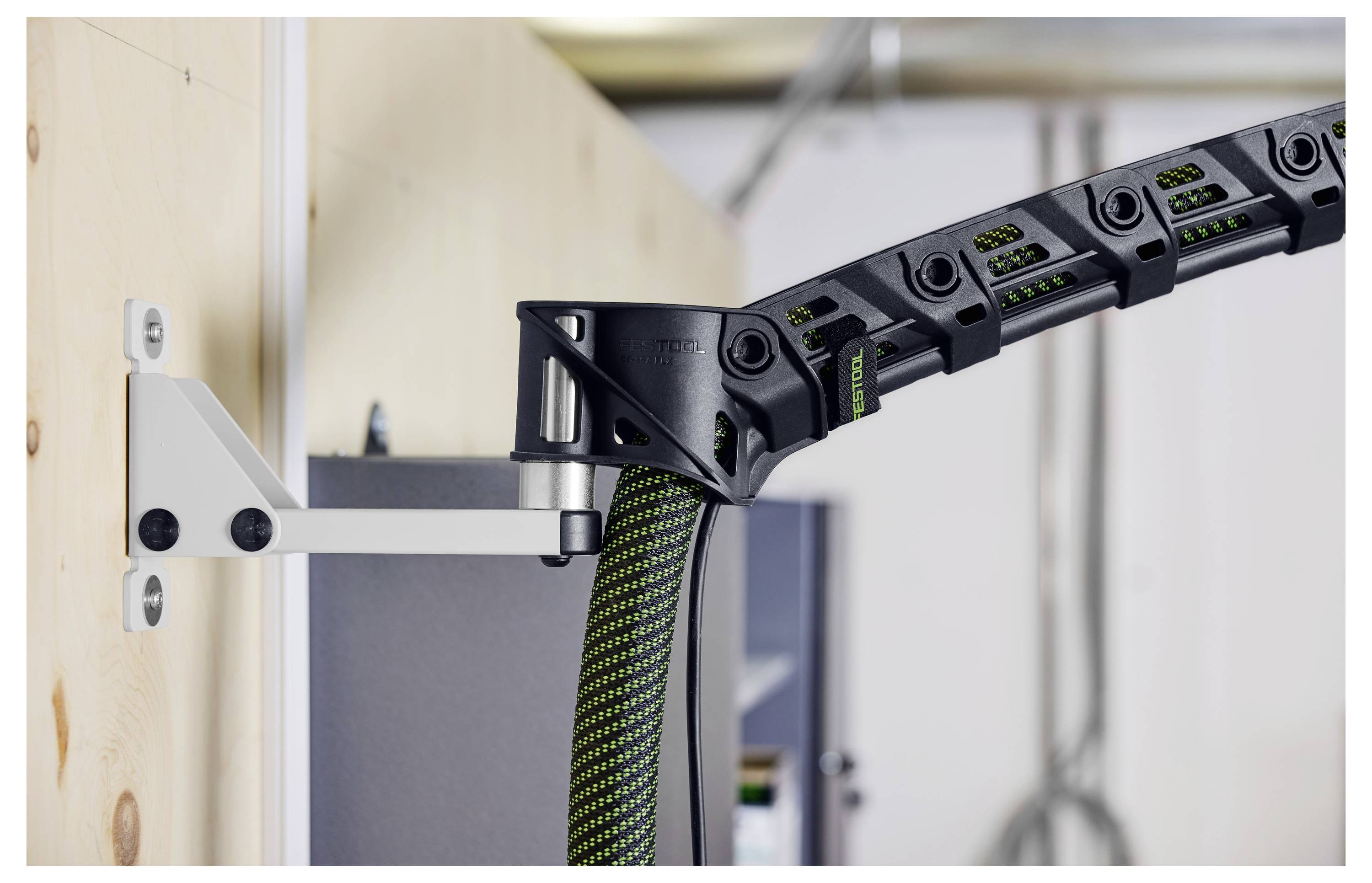 Ein Mann kniet auf einem Baustelle-Boden und montiert einen weißen tragbaren Staubabscheider. Die Umgebung zeigt unfertige Wände und Elektrokabel.