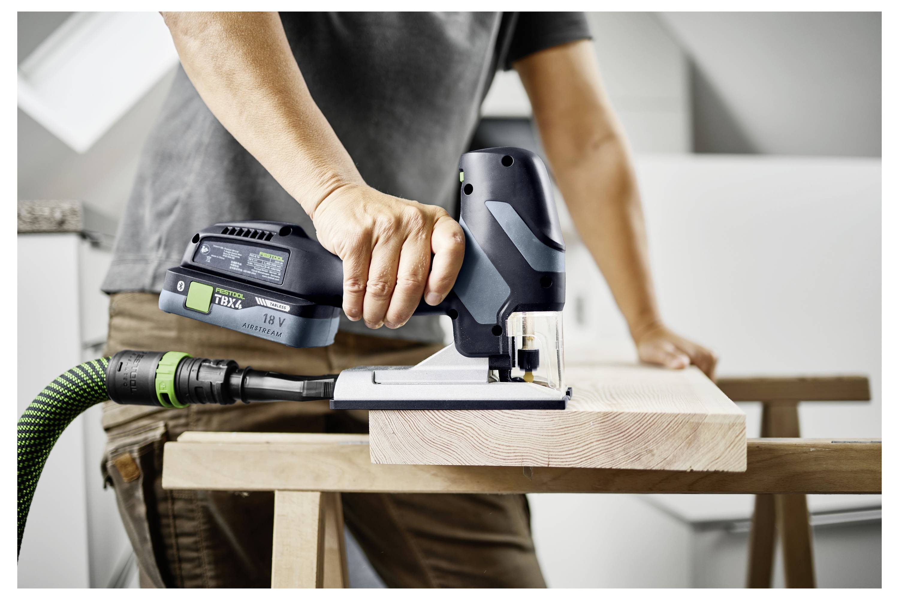 Eine Person benutzt eine kabellose Stichsäge, um ein Stück Holz auf einer Werkbank zu schneiden, wobei eine Heimwerker- oder Schreinertätigkeit demonstriert wird.