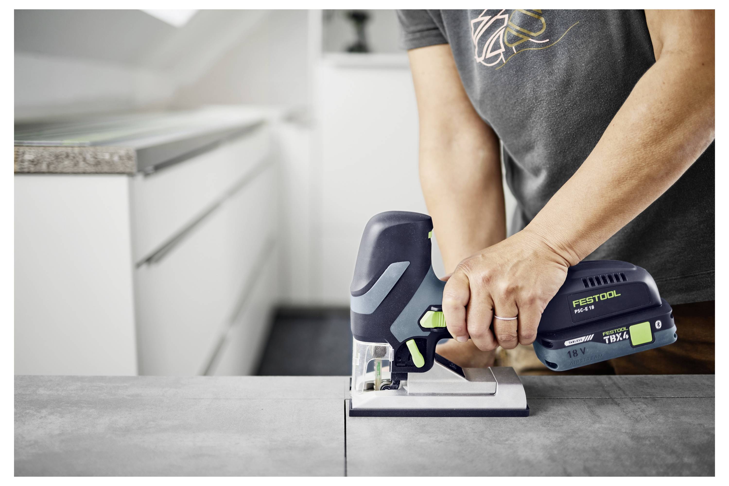 Eine Person schleift eine Wand mit einem langstieligen Werkzeug in einem Raum unter Konstruktion, wobei ein Staubsaugsystem angebracht ist, um Staub aufzufangen.