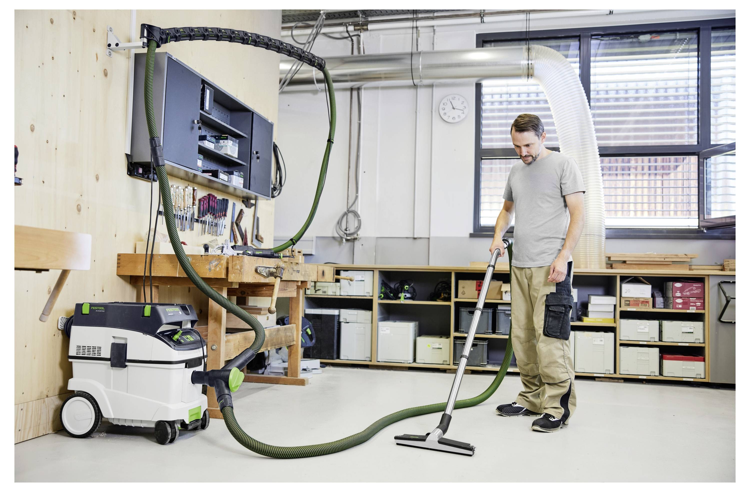 Eine Person trägt ein Festool-Hemd und eine Festool-Mütze und steht in einem Raum mit hellfarbigen Wänden und einem Fenster, blickend selbstbewusst nach vorne.