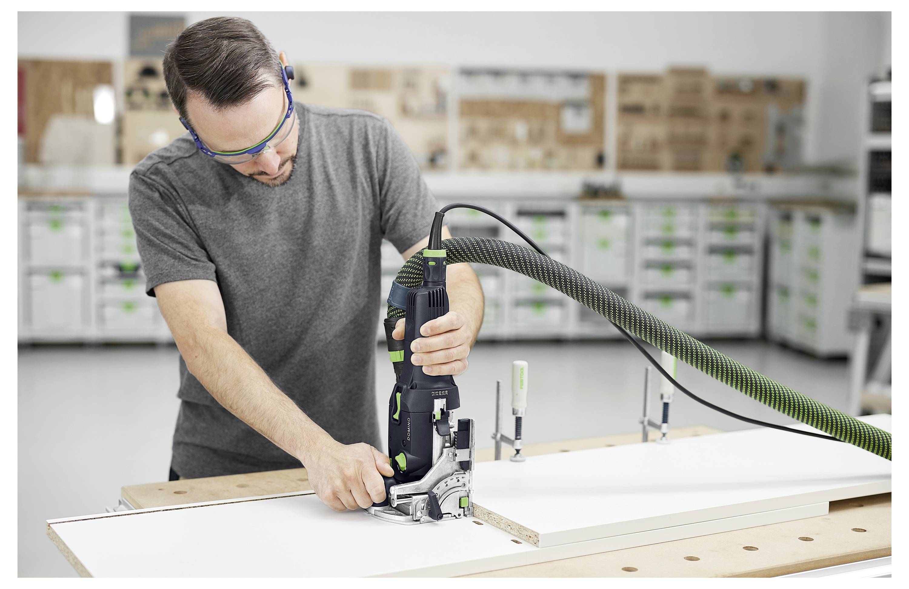 Eine Person, die eine Schutzbrille trägt, benutzt ein Elektrowerkzeug auf einer weißen Platte in einer Werkstatt und konzentriert sich auf präzises Schneiden.